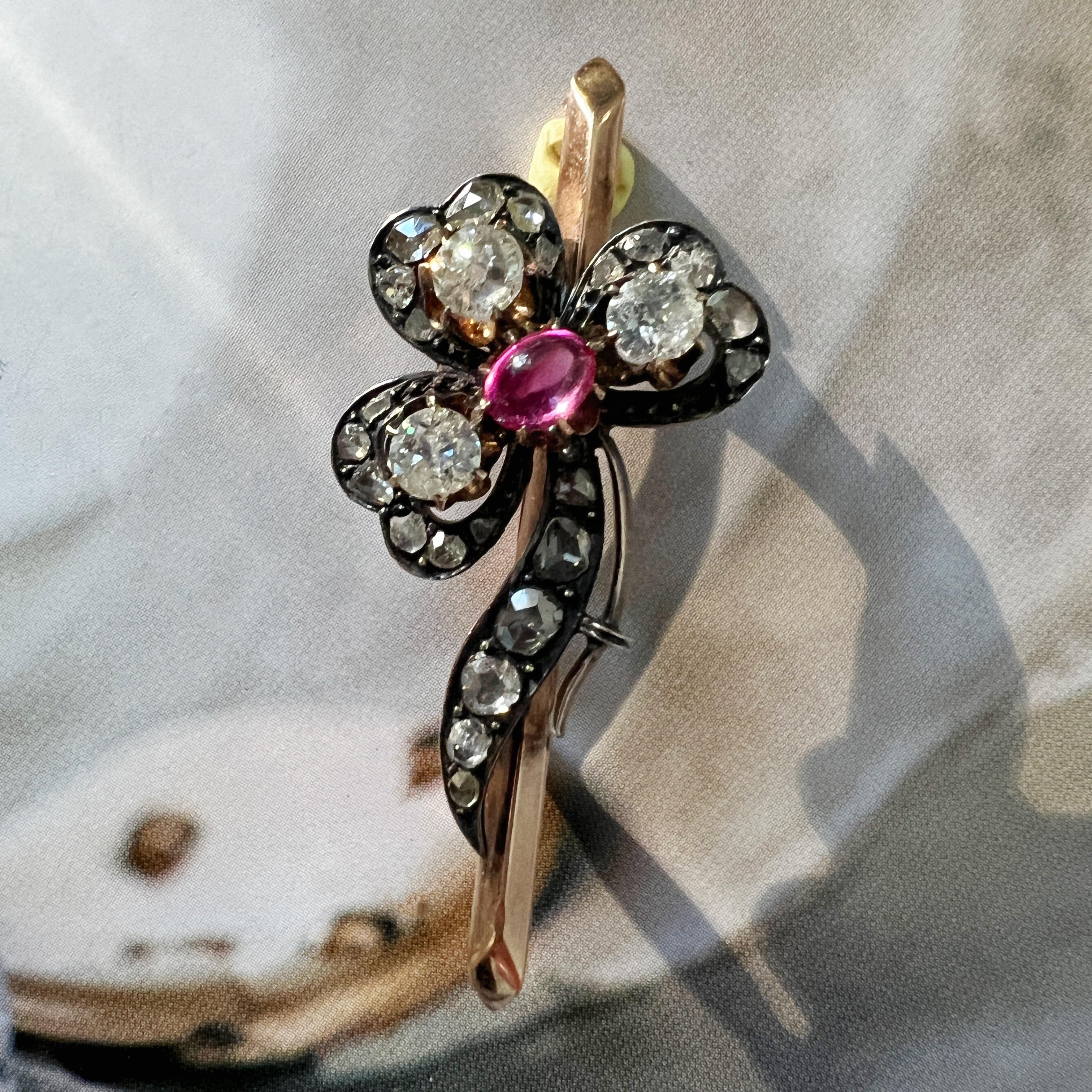 For sale a Victorian era 14K gold brooch, featuring a delicate three-leaf shamrock.

At the heart of the shamrock lies a vivid purplish-red ruby cabochon, radiating a rich and captivating hue. Surrounding the ruby are three old mine cut diamonds.