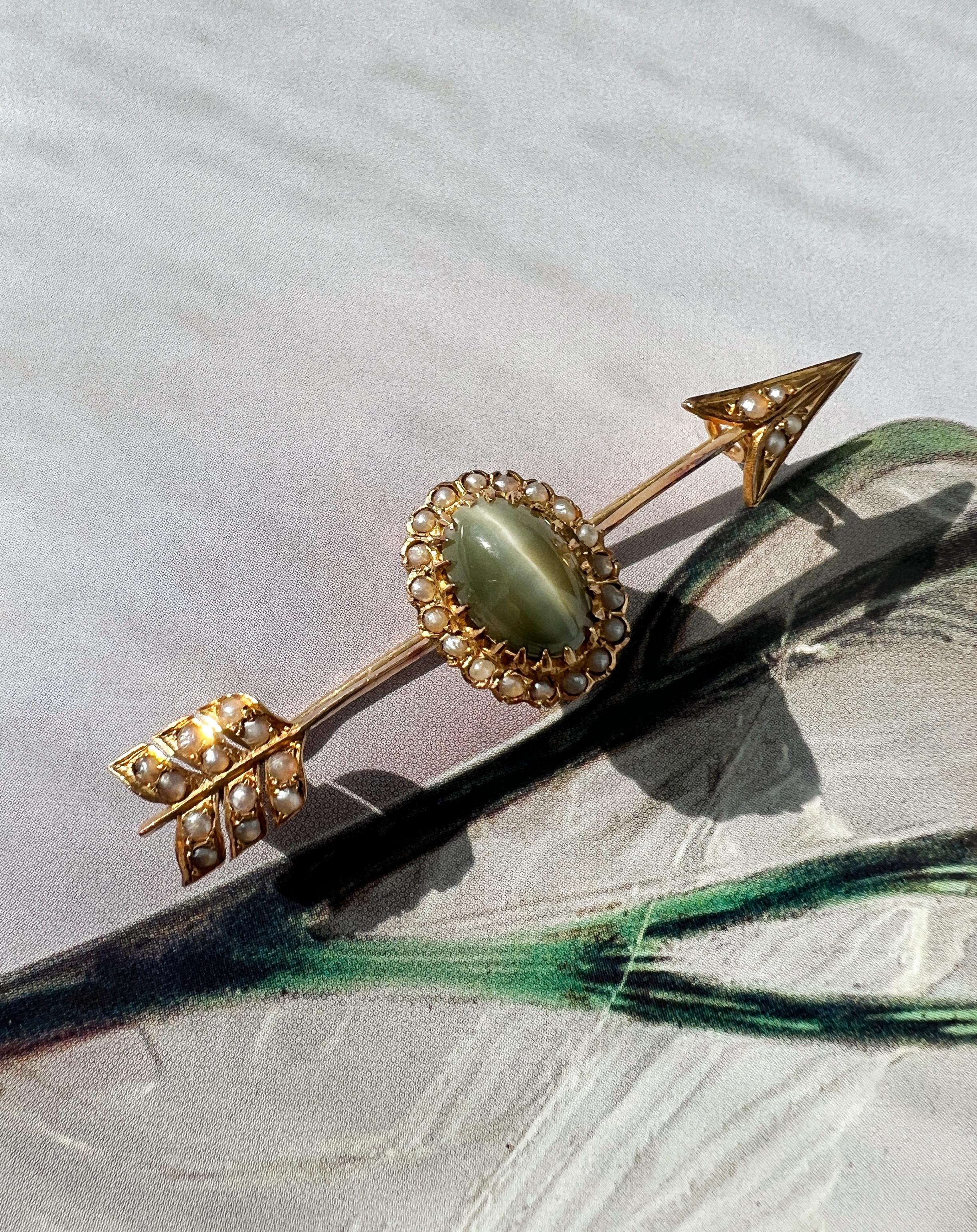 For sale a rare arrow brooch dated from the 19th century, the Victorian era. This brooch features a stunning yellowish-gray cat-eye chrysoberyl cabochon in the center: a precious phenomenon gemstone that displays a line in the center of the stone