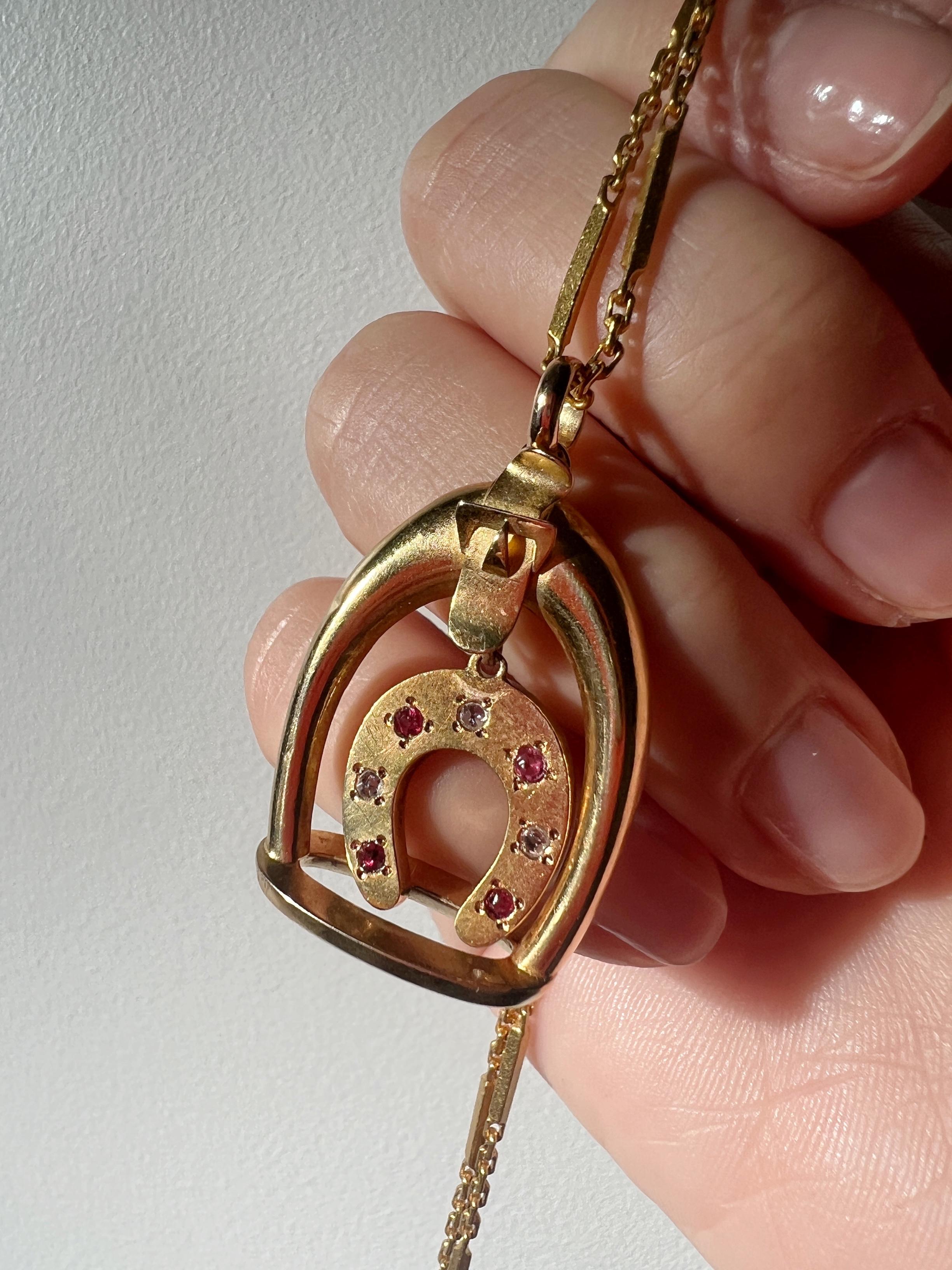 For sale a beautiful 18K gold pendant featuring a swinging horse shoe inside of a horse stirrup. On the horse shoe, there are 3 diamonds in rose cut style and 4 rubies in vivid pinkish red color.

The horse shoe / boot is considered as a symbol of