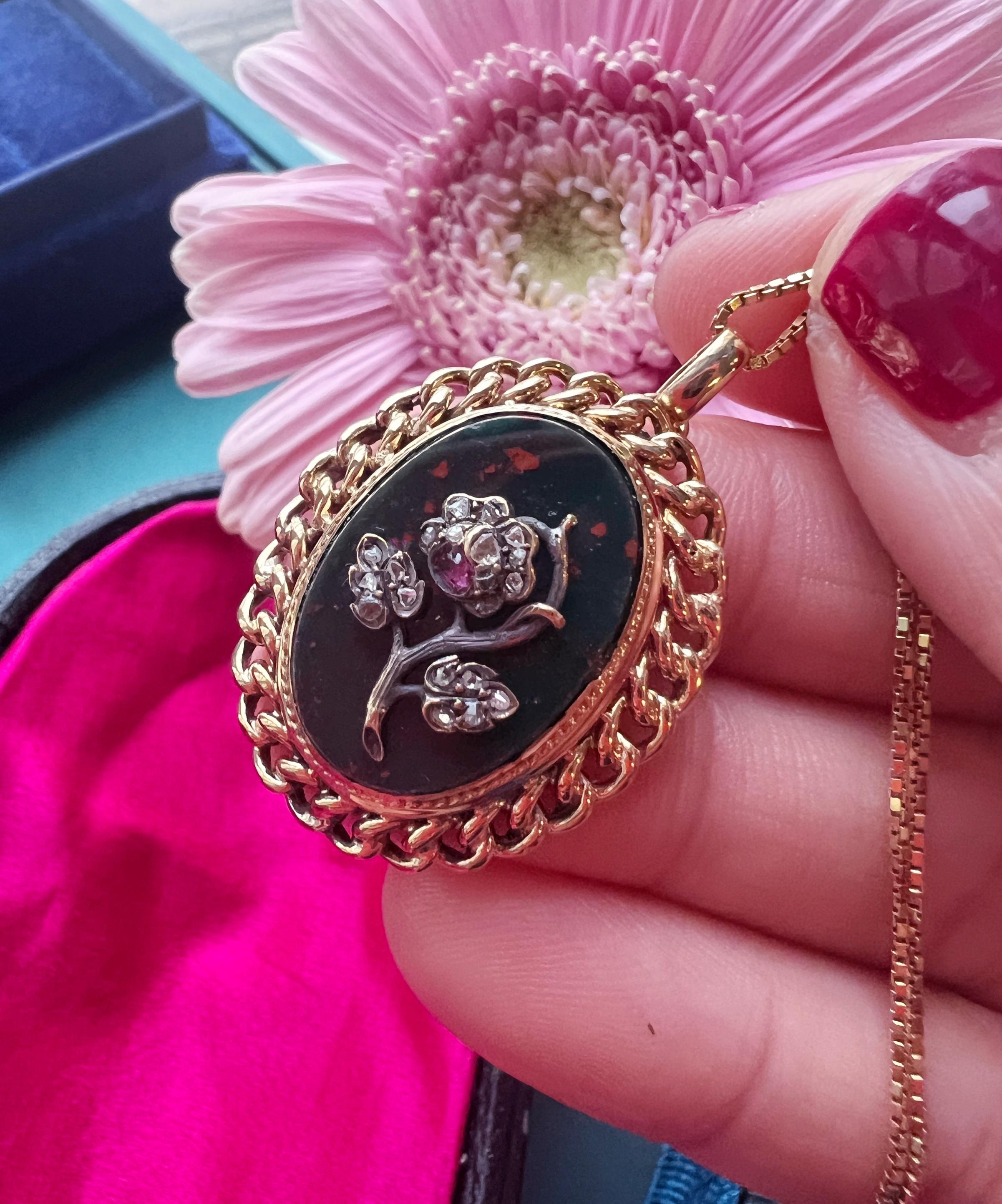 For sale a large 18K gold pendant featuring a rose flower entirely decorated with rose cut diamonds. There is a purplish red ruby in the center. The flower is piqué set on an oval-shaped, bloodstone panel, which conveys a deep green color with