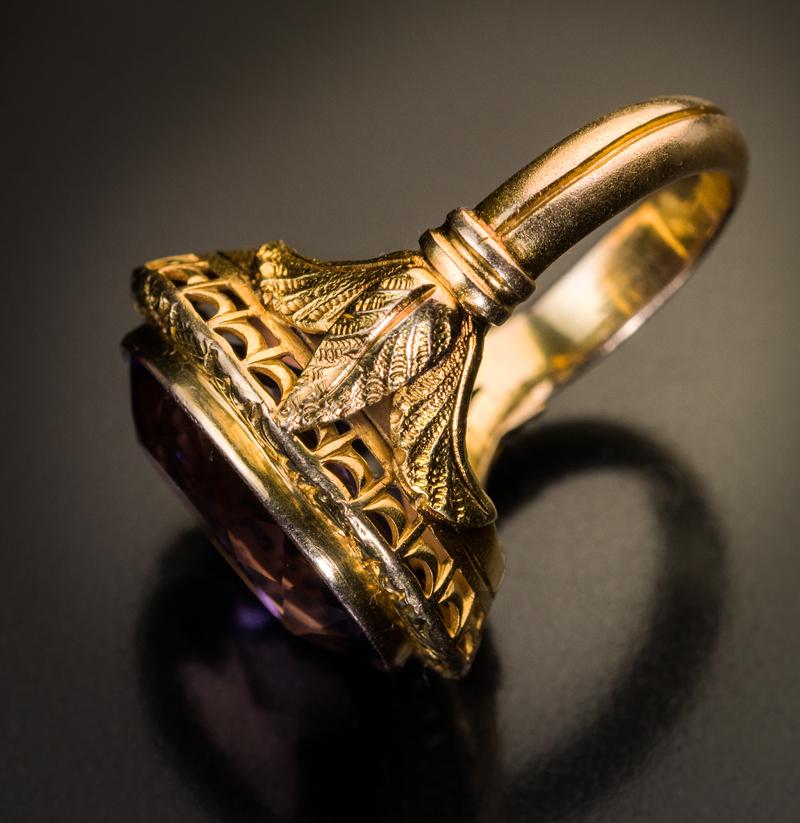 Circa 1880

This chunky antique gold ring features a large faceted amethyst set in an ornate chased bezel flanked by stylized palm leaves.

The bezel measures 26 x 20 mm (1 x 13/16 in.)

Height of the setting including the amethyst is 9 mm (3/8