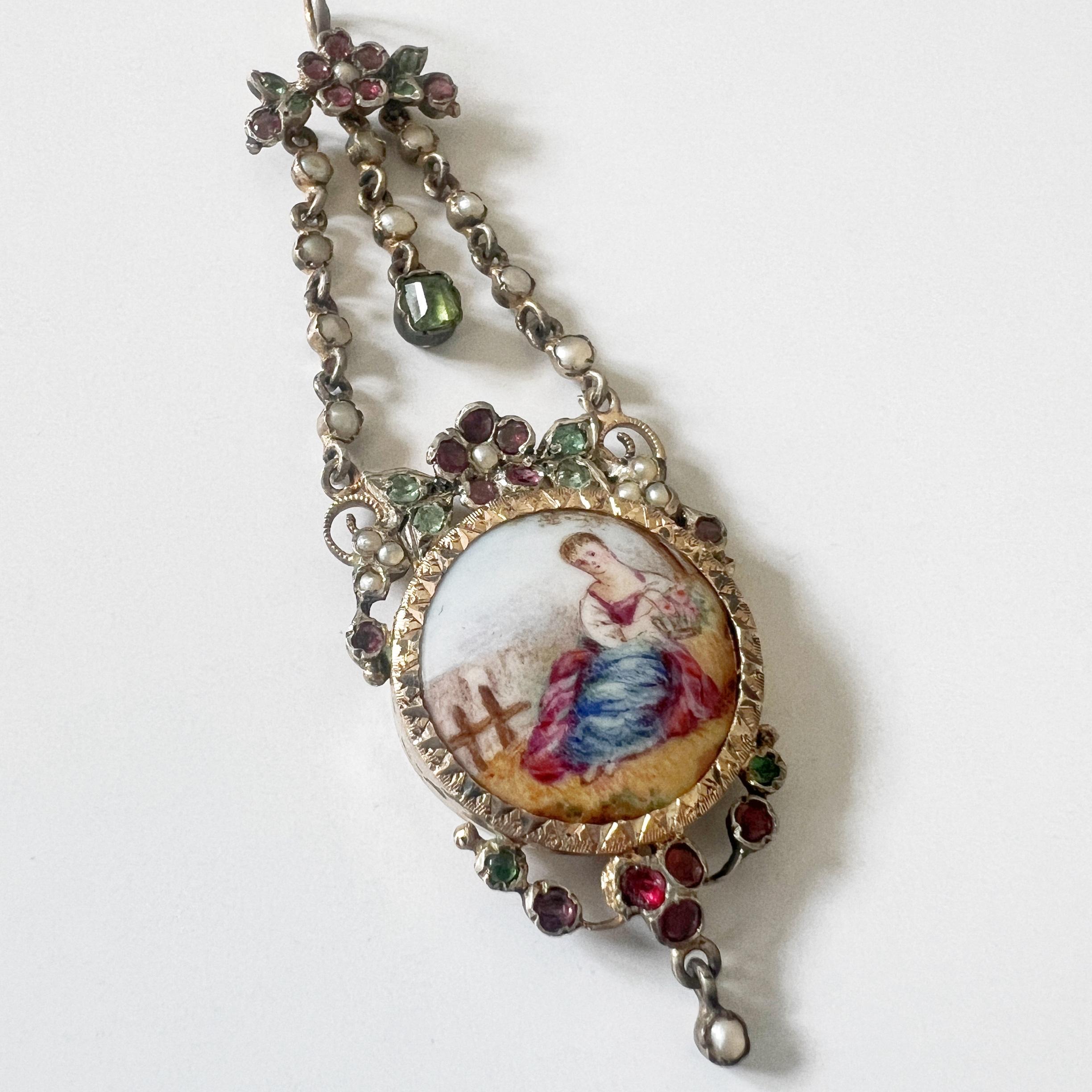 For sale a beautiful Victorian era miniature portrait pendant, featuring a round enamel panel capturing the image of a young girl, adorned in a captivating long dress in delicate shades of pink and blue.

The young girl's hands, delicately holding a