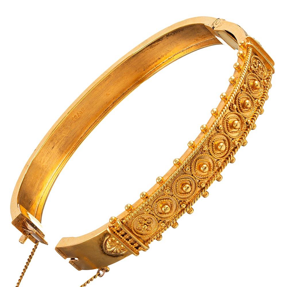 Created of 15 and 18 karat yellow gold, this slender bangle is intricately decorated with Etruscan revival style granulation and an artful pattern of golden wirework. The interior diameter measures 2.25 by just under 2 inches. The bracelet is just