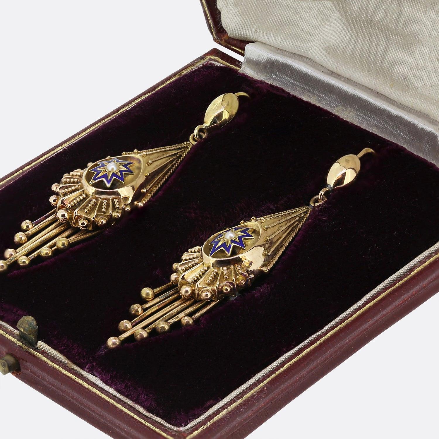 This is a pair of Victorian 18ct yellow gold drop earrings. The earrings are crafted in an etruscan style and feature a central blue enamel star set with a pearl in the centre. At the bottom of the of the earrings there are seven drop sections that