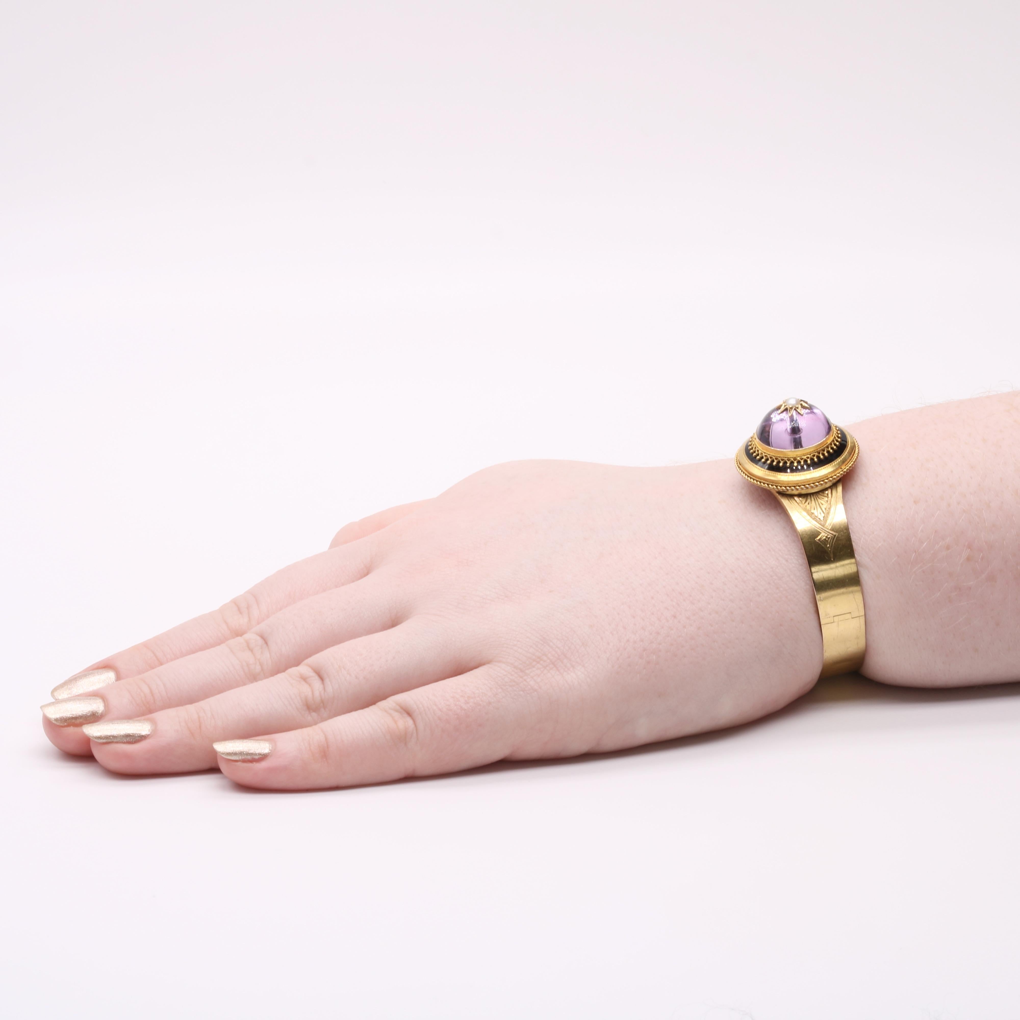An antique gold, amethyst, pearl and enamel bracelet set with a cabochon amethyst, one seed pearl and adorned with black enamel, crafted from 18 karat yellow gold.  

The high domed amethyst cabochon is a beautiful lilac hue, which appears as a