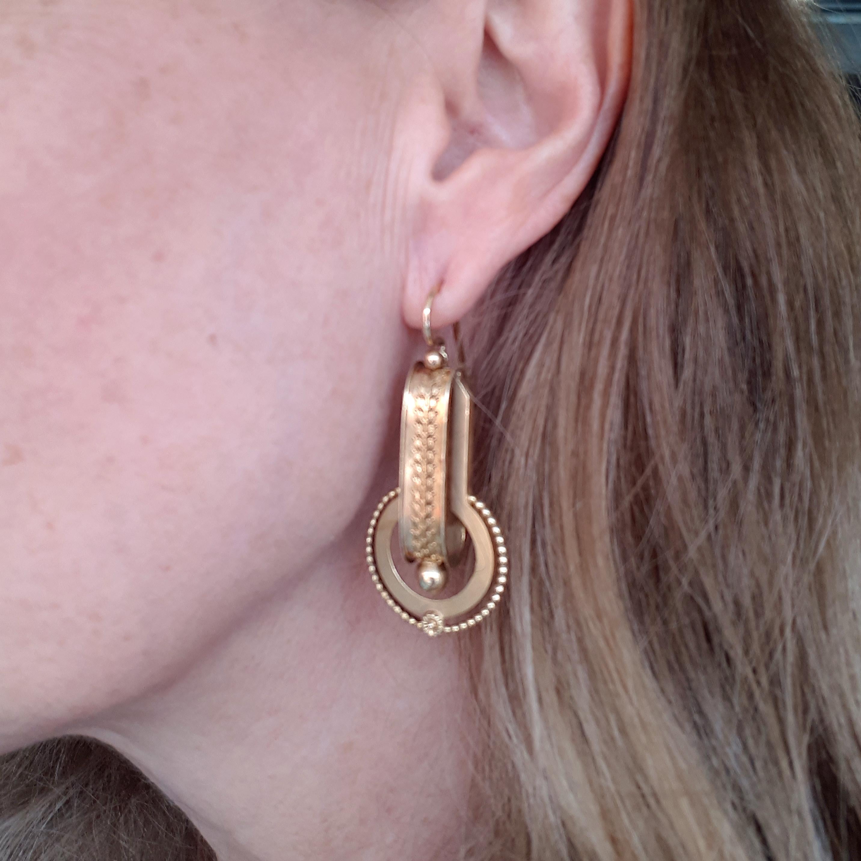 A Victorian gold Etruscan Revival suite, comprising a brooch, with pendant fitting and a matching pair of drop earrings, with Etruscan style work decoration, on articulated sections, with inventory mark number 4381, circa 1875. Electronically tests