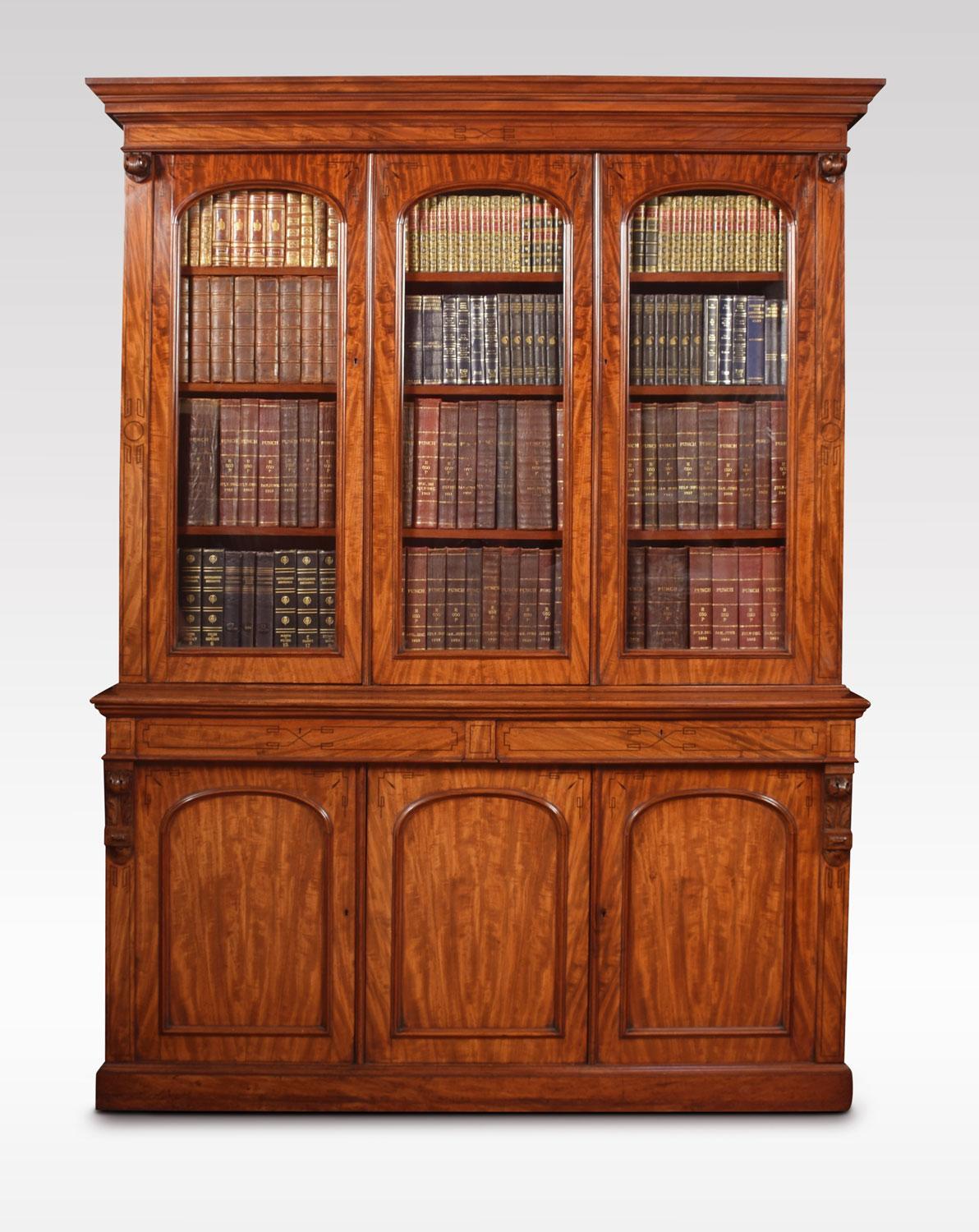 Victorian figured mahogany library bookcase, with overall line inlaid ebony borders. The moulded pediment above three arched glazed doors opening to reveal adjustable shelved interior. To the base fitted with two frieze drawers and three arched