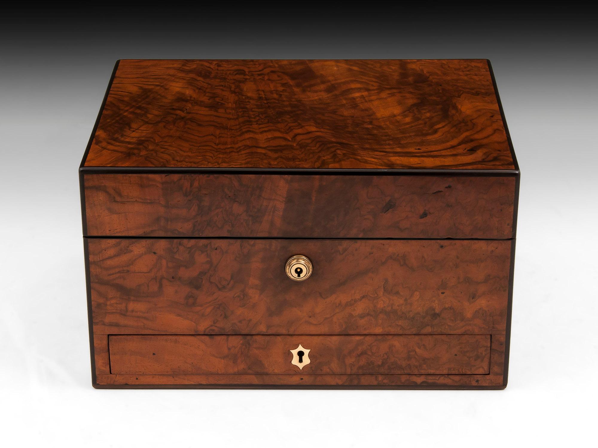 Beautiful figured walnut jewelry box with ebony edging and brass escutcheons. 

The interior of this jewelry box is lined with maroon velvet and silk paper and features a removable tray with several compartments including one for rings, earrings