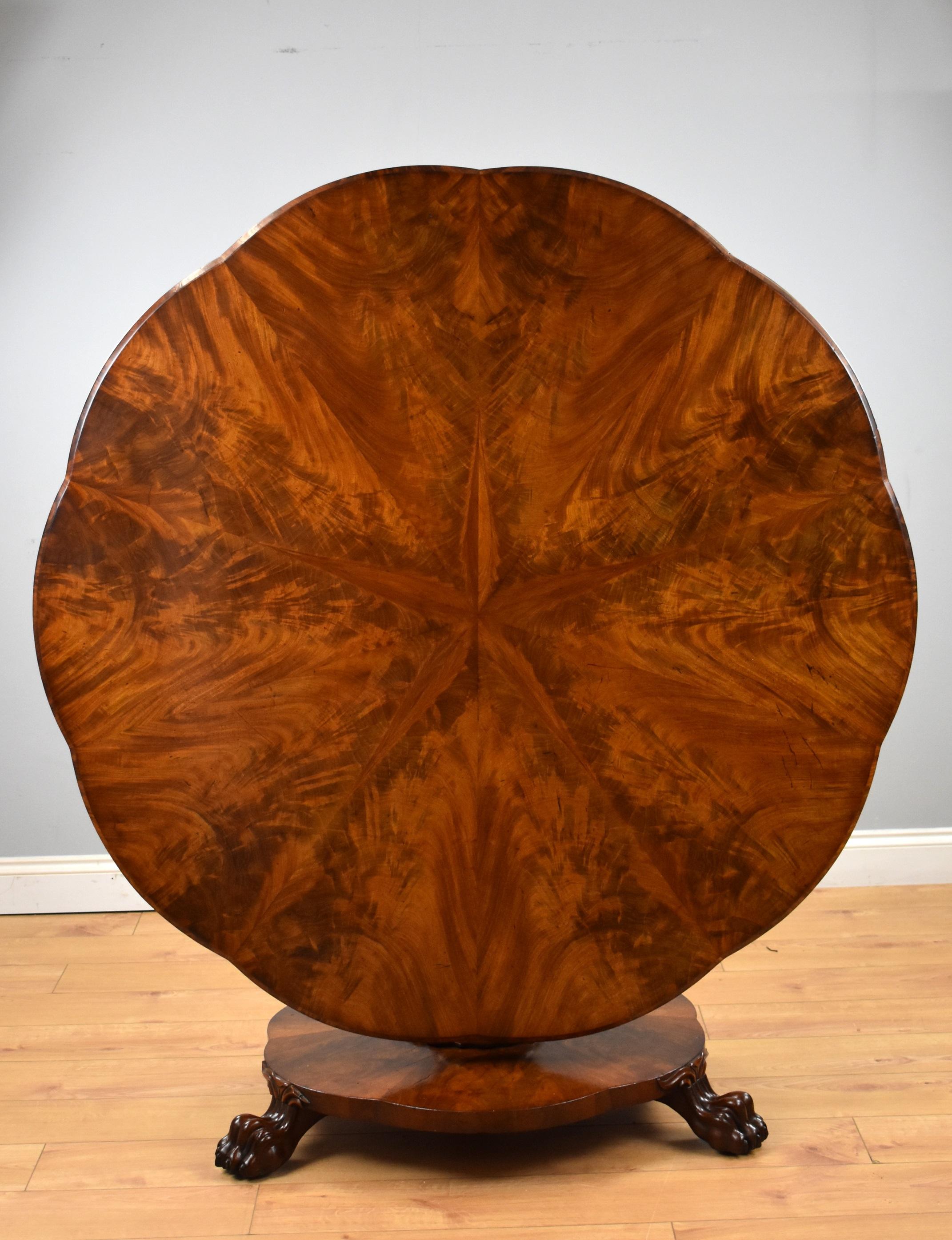 For sale is a fine quality early Victorian flame mahogany breakfast table, having a shaped and chamfered top, with radial starburst figured mahogany veneer, with a vase shaped faceted column above a shaped platform base raised on lions paw feet. The