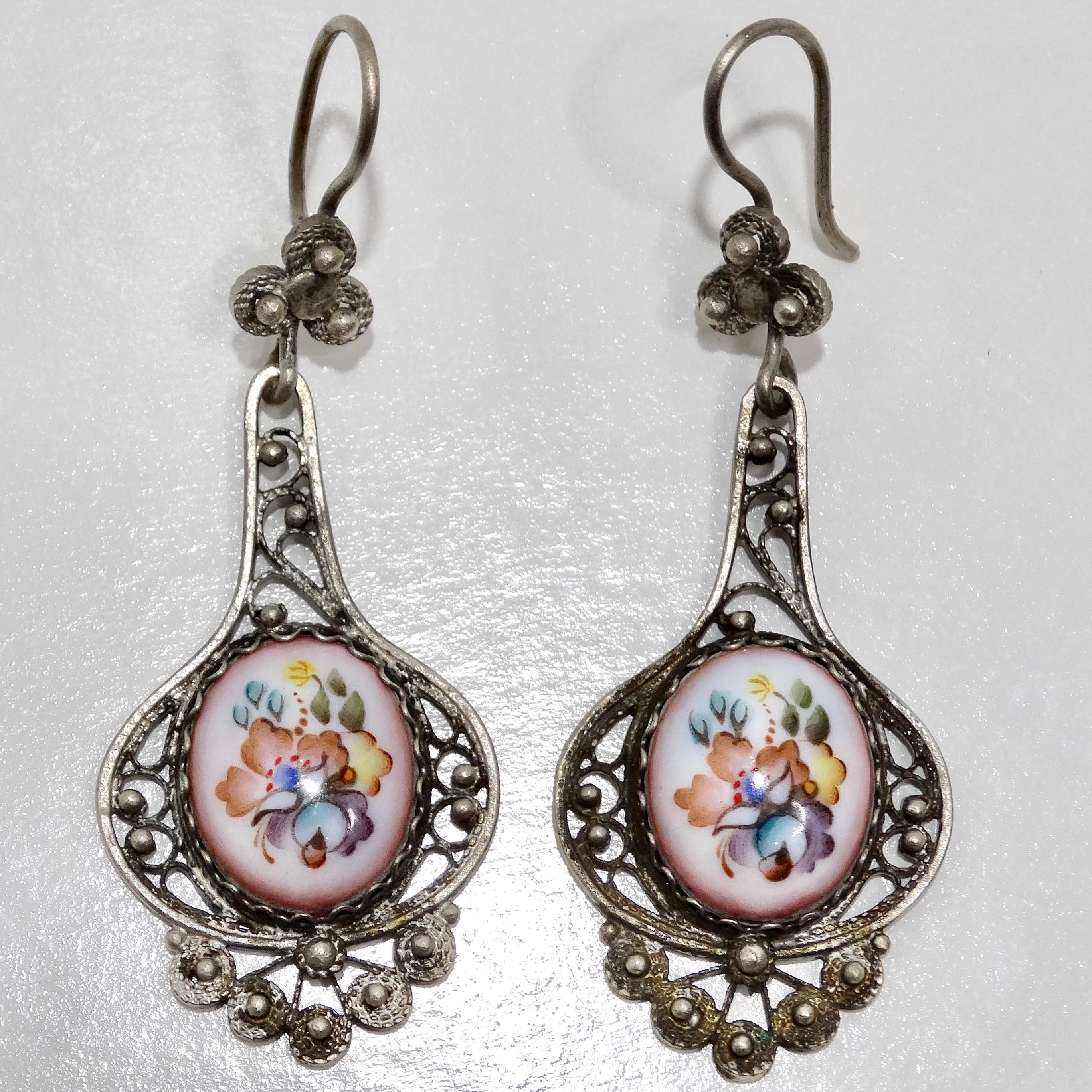 Experience the timeless charm of the Antique Victorian Floral Porcelain Dangle Earrings, a beautiful pair of earrings that encapsulates the elegance and artistry of a bygone era. These exquisite 1940s silver dangle earrings feature delicate