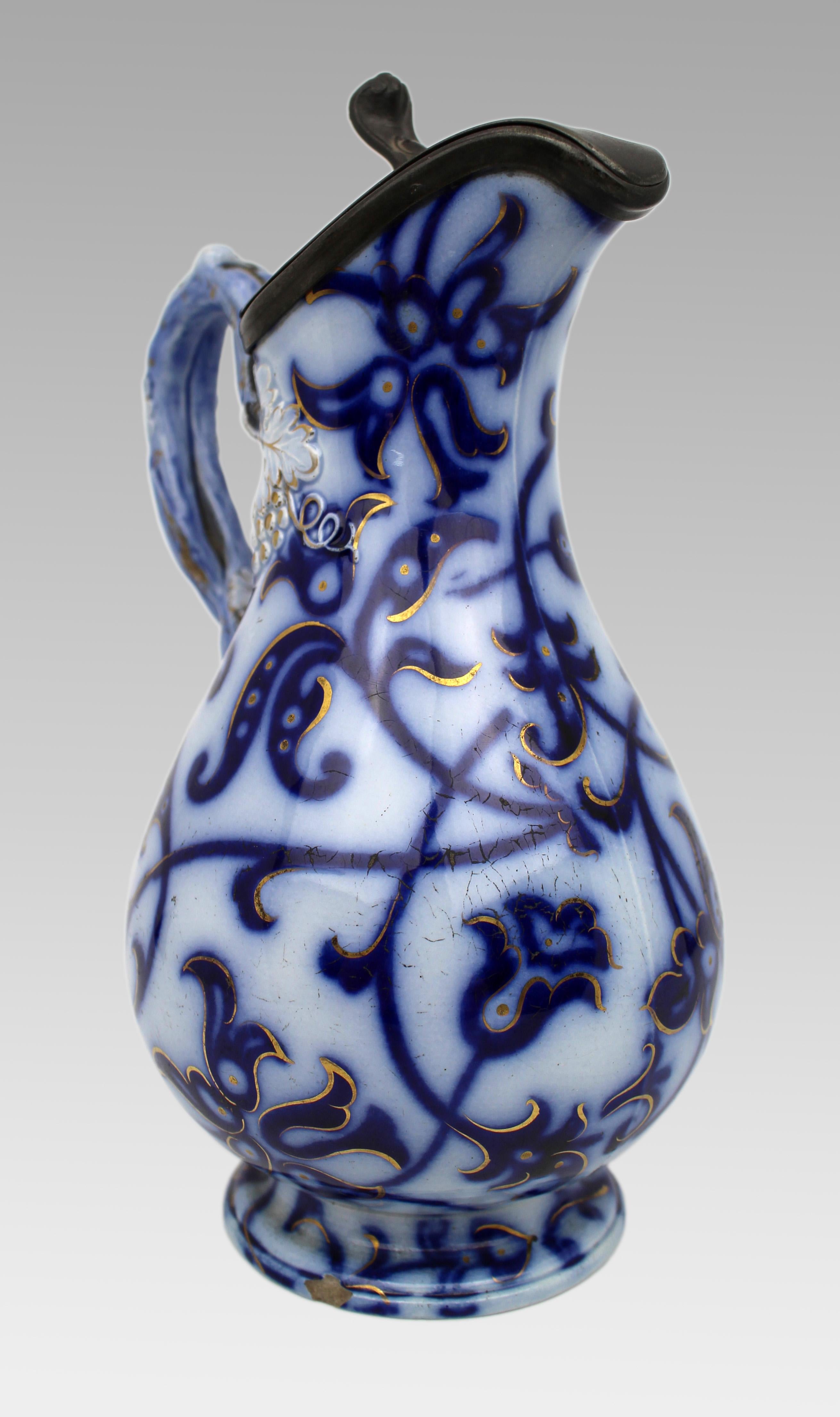 Victorian Flow Blue and Gilded Ceramic Jug with Pewter Lid, England, circa 1850
A decorative mid-19th century English ceramic jug, finely decorated in the Flow Blue tradition with scrolling foliate motifs and hand-applied gilt highlights. The
