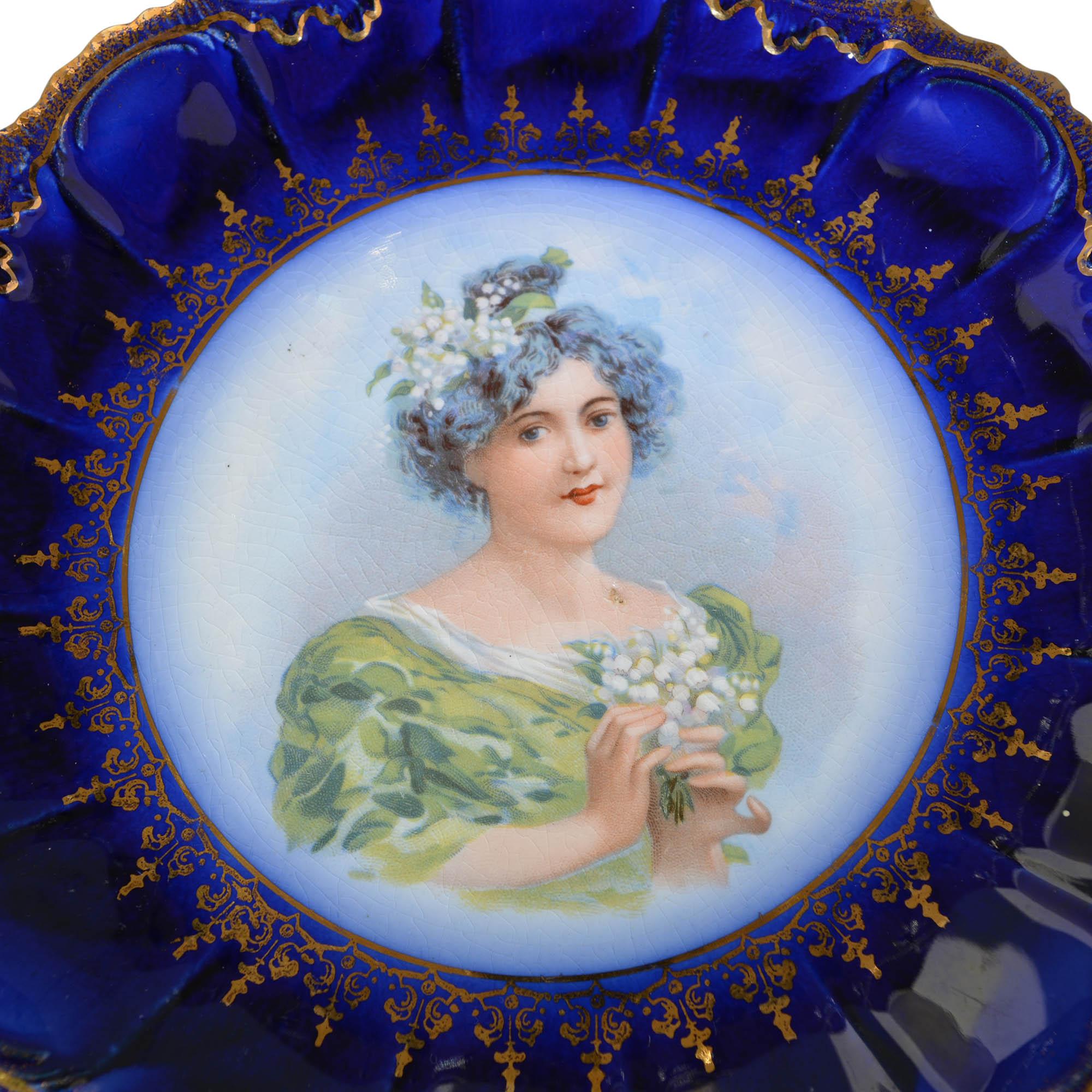 The deep, royal blue rim of the flow blue plate is beautifully accented with rich gold trim along the scalloped edges. The center reflects an amazingly hand painted portrait of a lovely lady with a bouquet of flowers in fine detail. 

Marked on