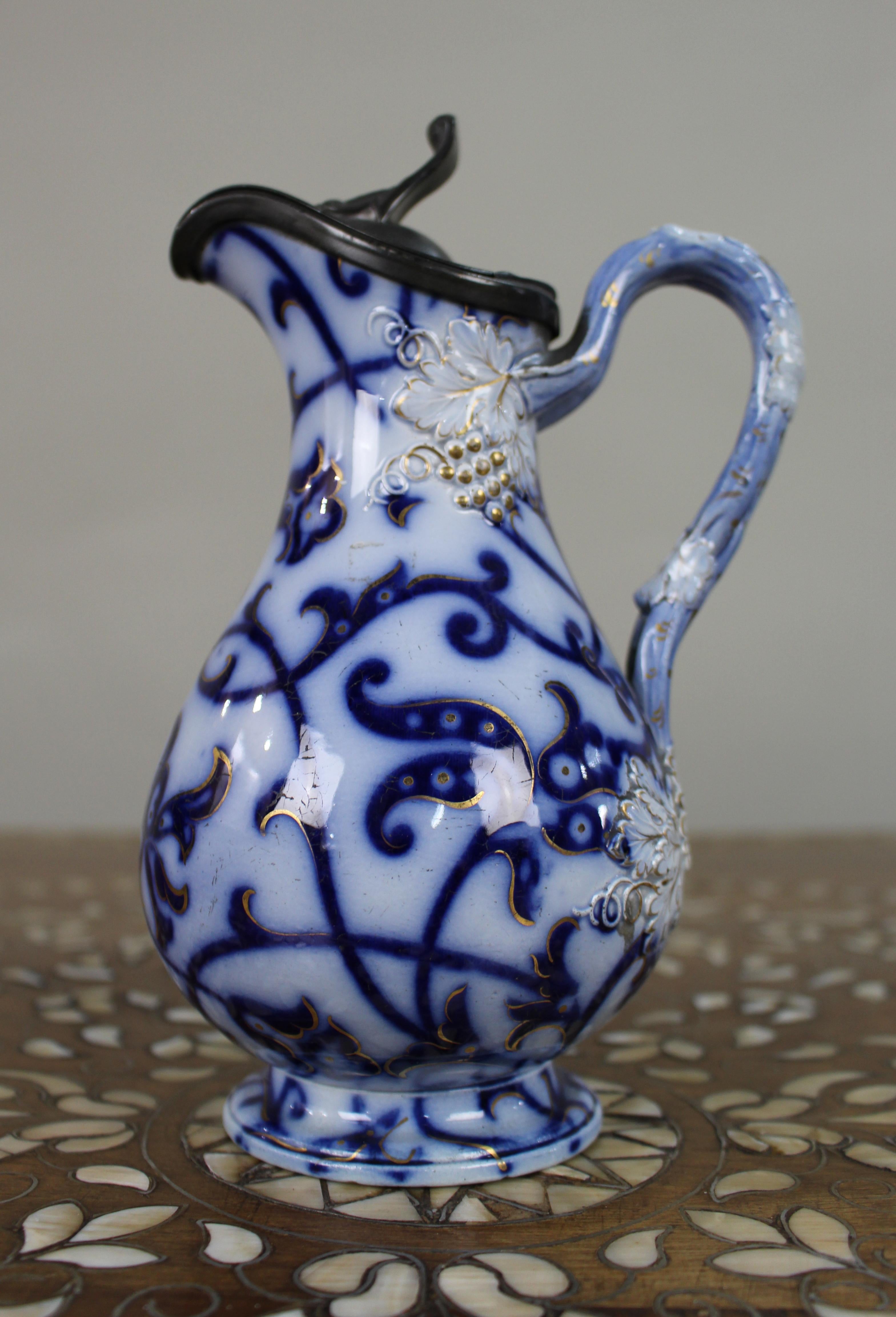 Brocca vittoriana in ceramica blu e dorata con coperchio in peltro, Inghilterra, circa 1850
Brocca decorativa in ceramica inglese della metà del XIX secolo, finemente decorata secondo la tradizione Flow Blue con motivi fogliati a volute e