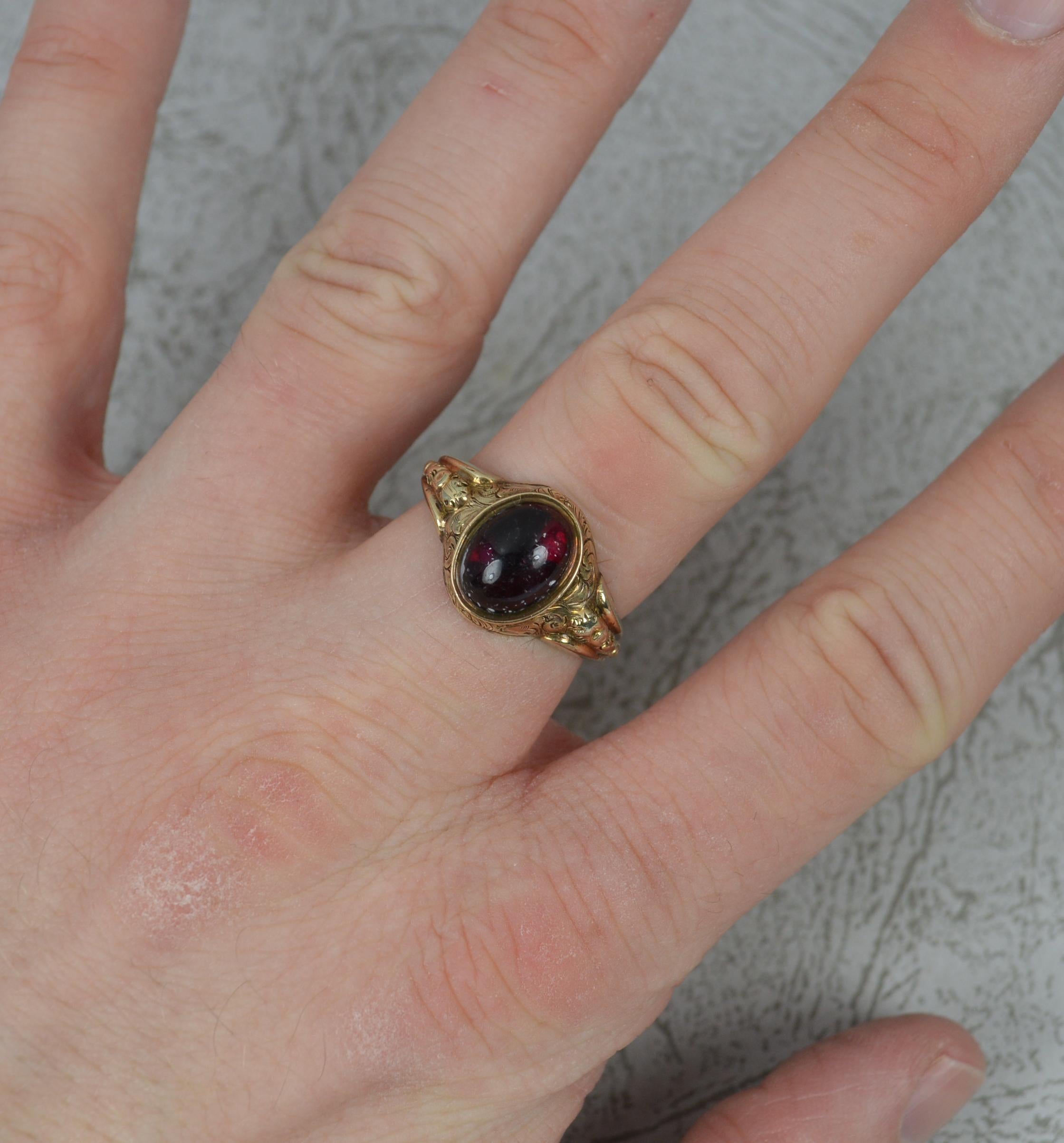 A fine mid Victorian era ring.
Designed with an oval shaped garnet cabochon to centre, 7mm x 10mm approx.
Set into a hollow 9 carat yellow gold shank with fine floral engraving surrounding the head and shoulders.

CONDITION ; Very Good for age. Well