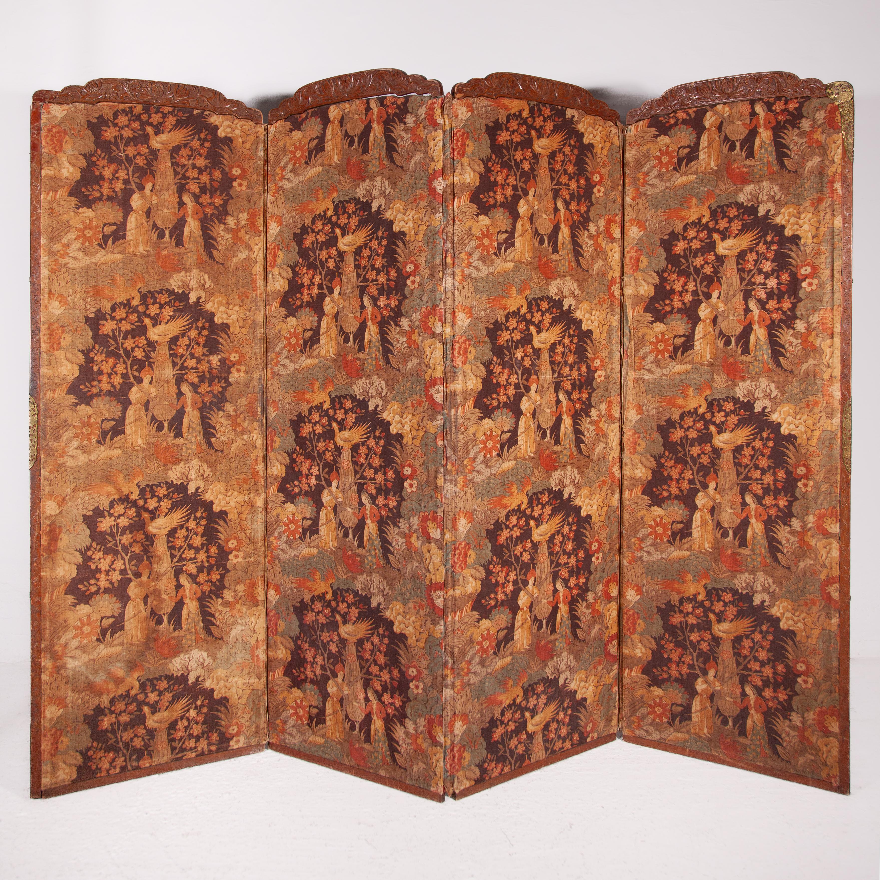 Paravent victorien à quatre panneaux du XIXe siècle, encadré de bois sculpté avec des fleurs de lotus et terminé par des éléments décoratifs en laiton. Les panneaux sont tapissés d'un motif textile exotique et poétique, répété dans des tons de terre