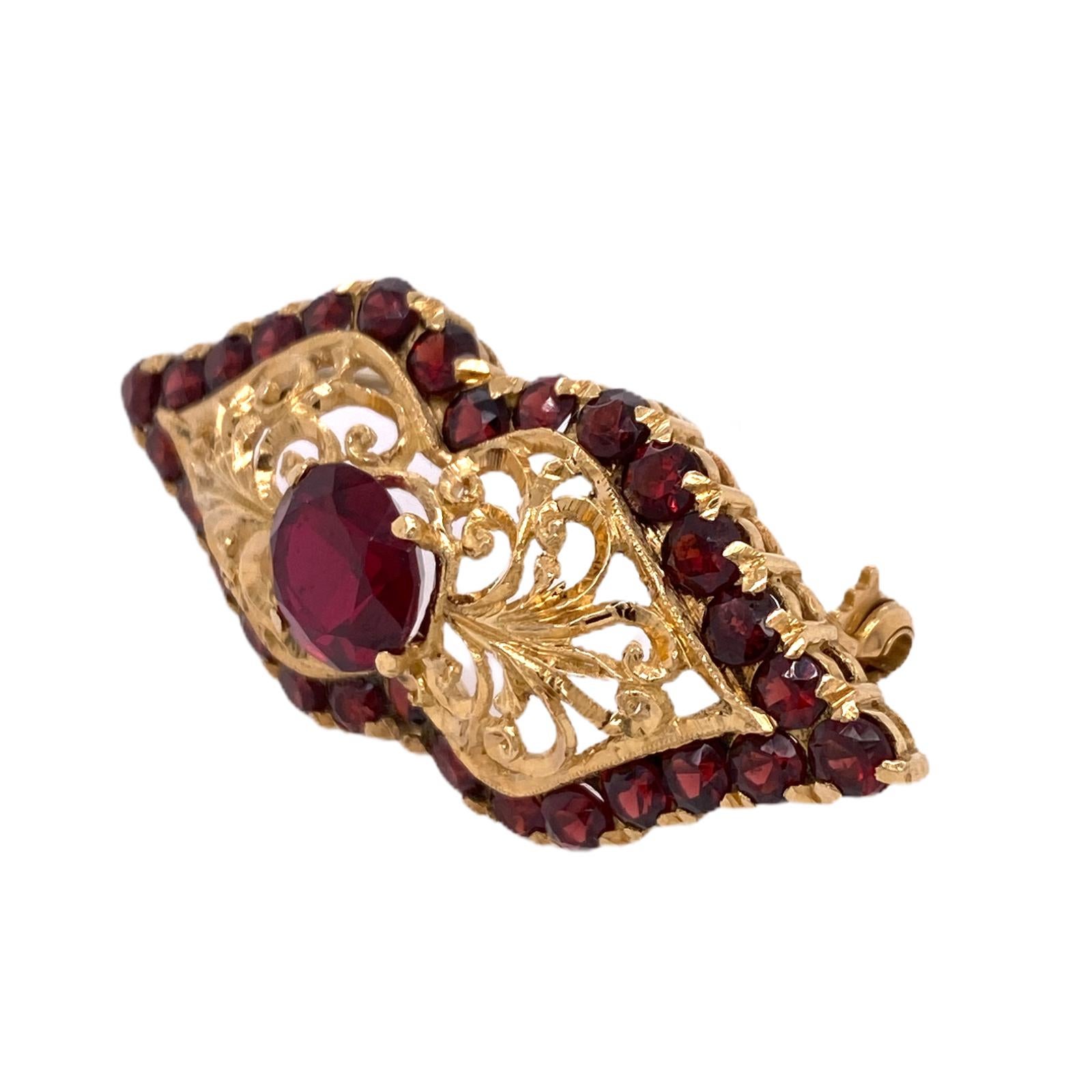 Beautiful Victorian brooch hand crafted in 18 karat yellow gold. The antique pin features red garnet gemstones and hand carved open gold design. Measures 20 x 50mm. 
