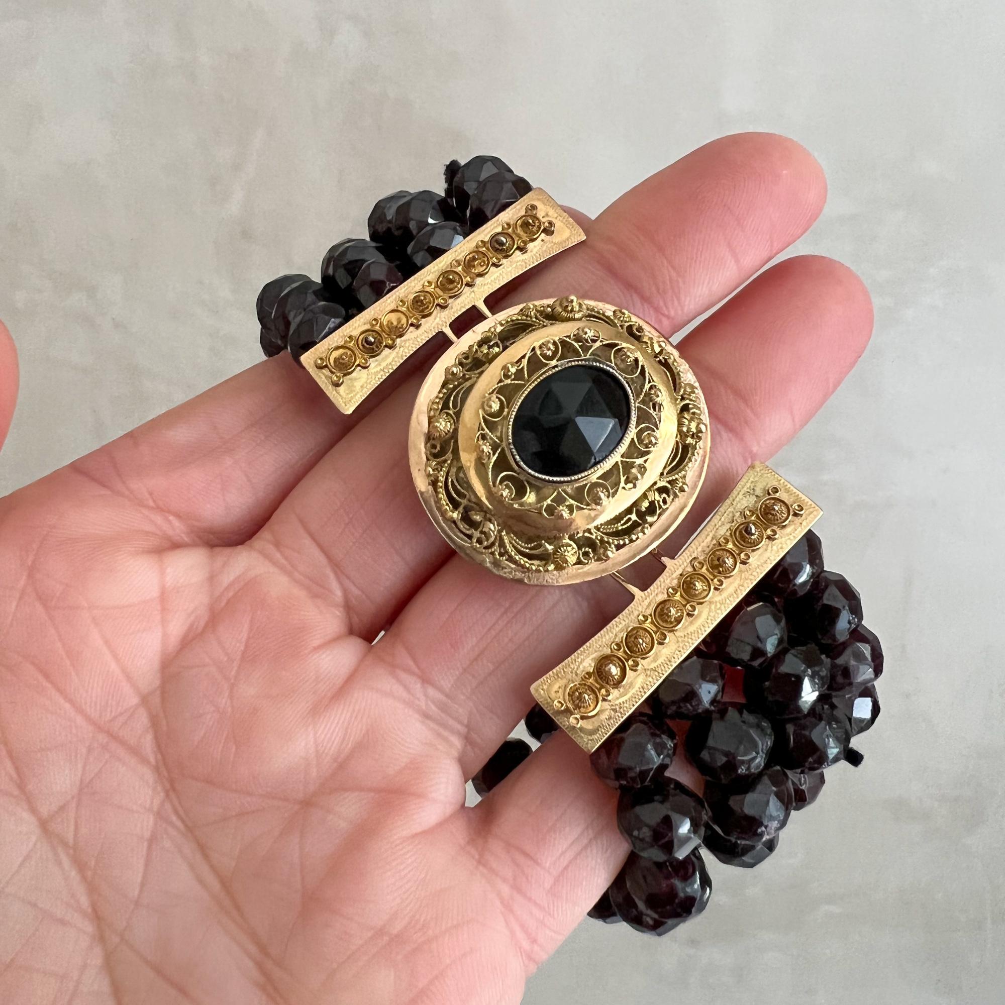 This is an antique 14 karat gold multi-strand beaded garnet bracelet. The bracelet is made of four strands and made with a beautifully handmade golden filigree clasp. In the center of the clasp a large oval-shape garnet stone is set in gold bezel