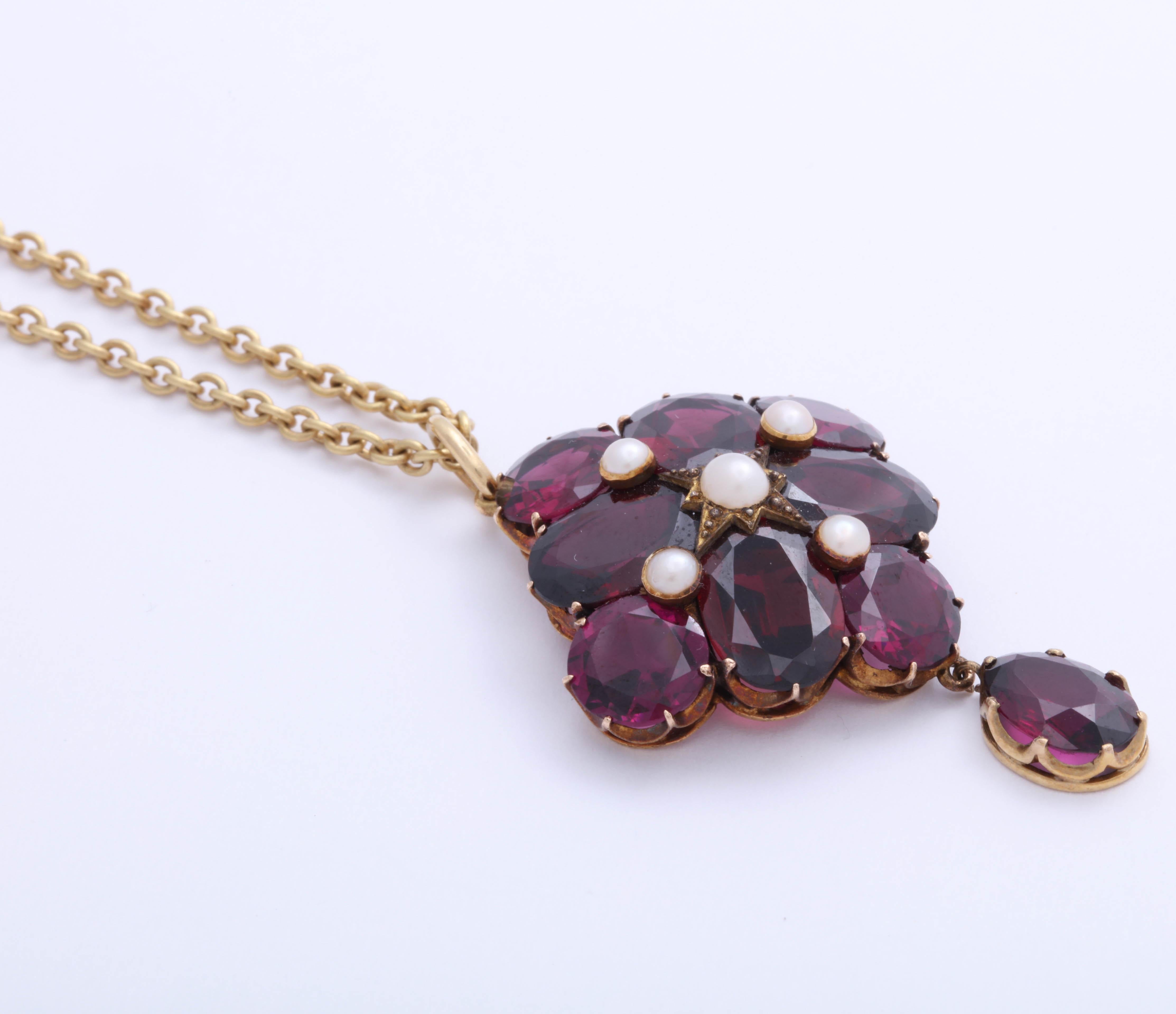 Lovely almandine garnets set in yellow gold with one garnet dangle. 5 natural pearls. A small locket compartment in the center of the back of the pendant. On yellow gold chain. 