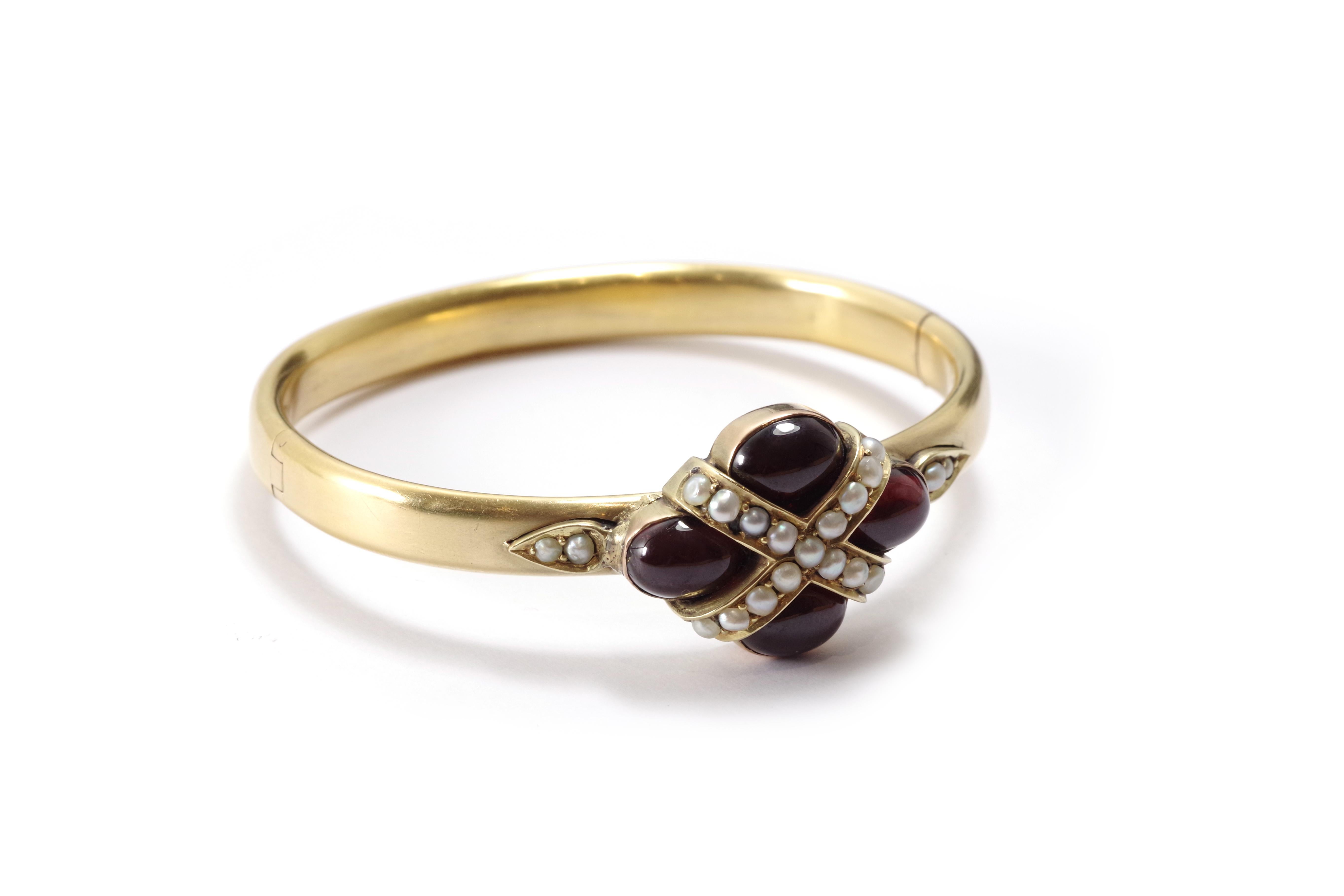 Victorian garnet bangle bracelet in 18k rose gold. Bangle bracelet featuring a central element set with four large cabochon almandine garnets, topped with a cross set with 18 fine pearls. A drop-shaped motif set with fine pearls complements the main