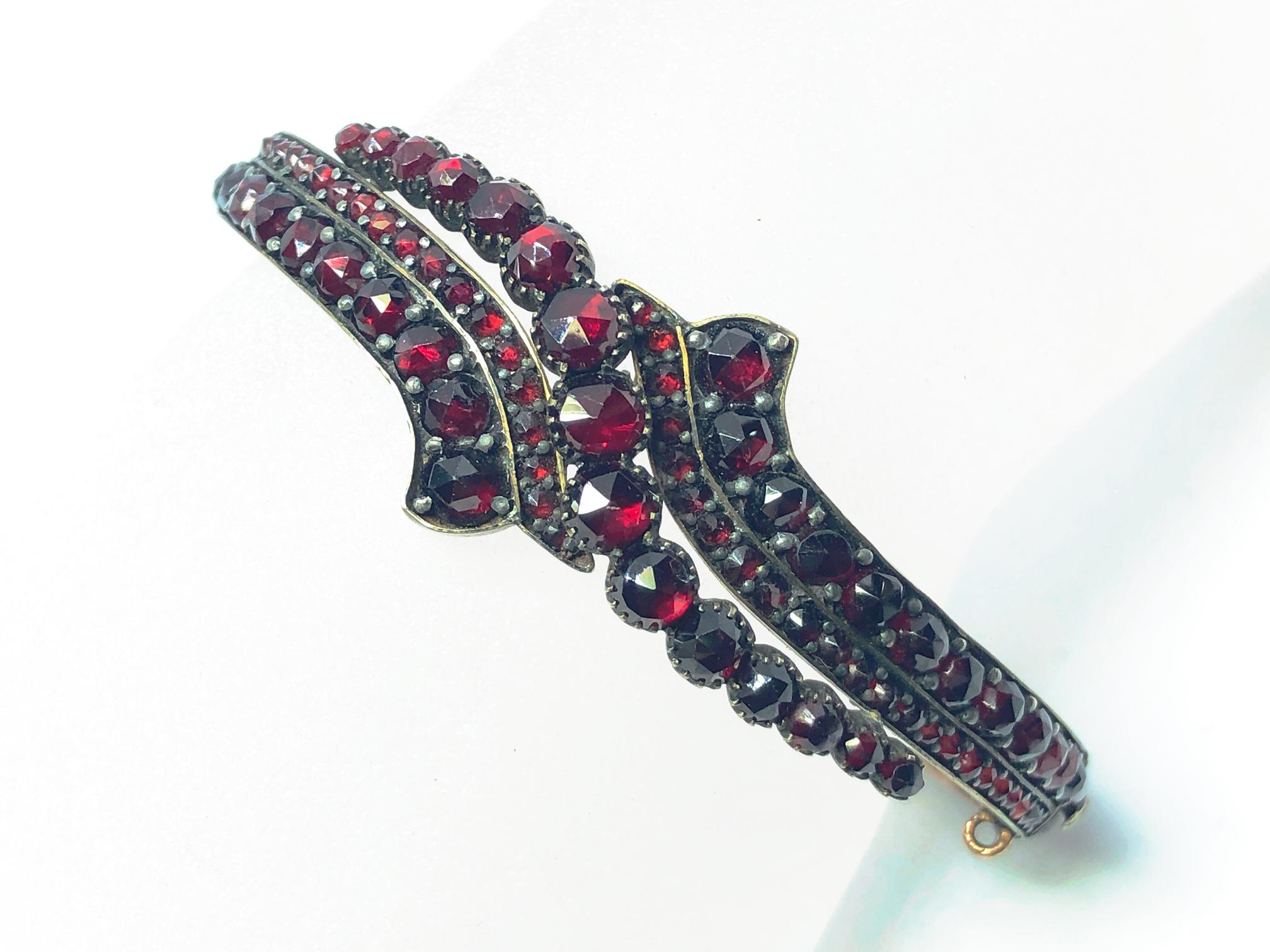 Victorian Bohemian garnet clasp bangle, rose cut garnets set in a crossover design to the full hoop, claw set in yellow metal, push clasp. Circa 1860.