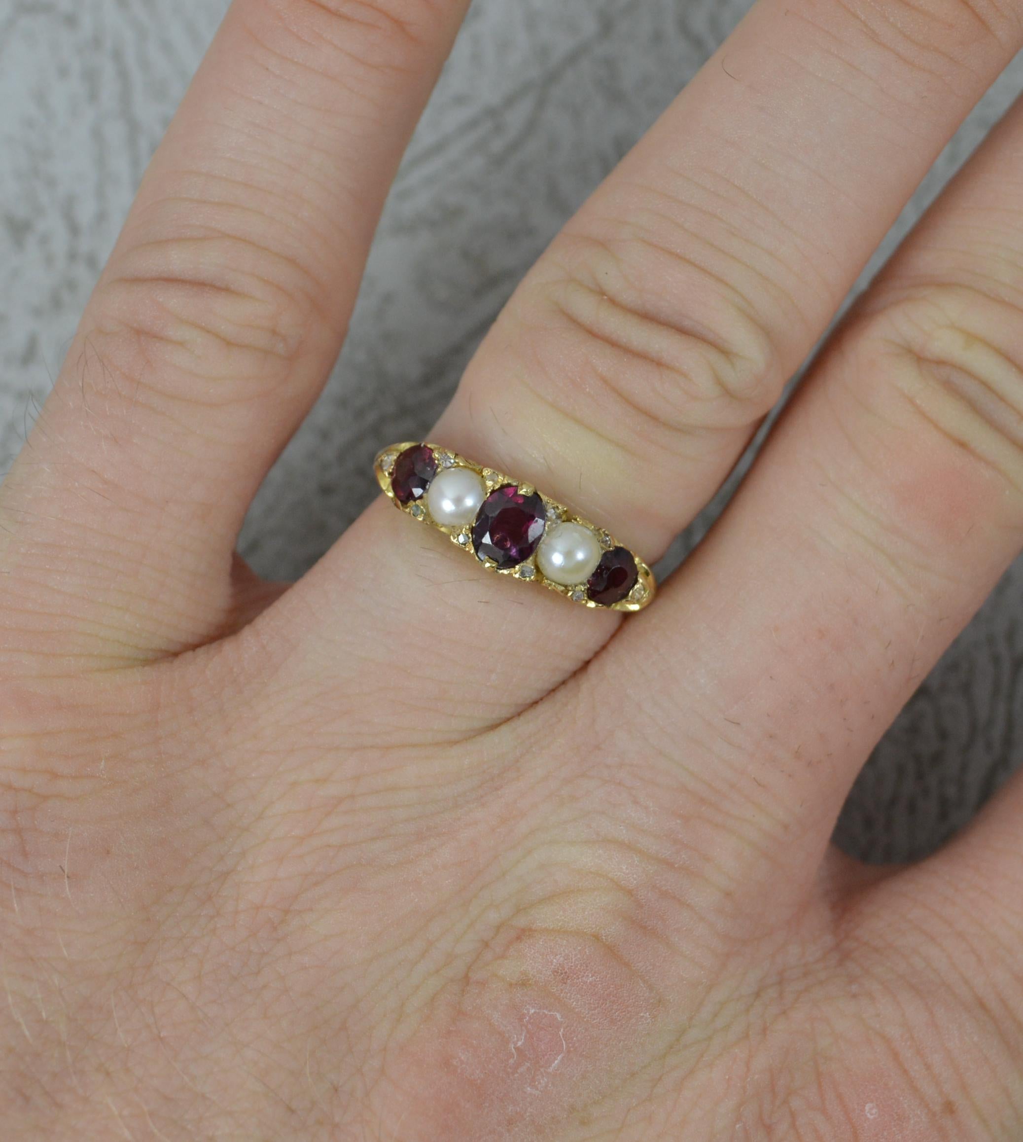 A fine 18 carat gold, garnet, pearl and diamond five stone ring. c1880.
18 carat yellow gold shank and setting with deep floral scroll work.
Designed with alternating natural almandine garnets and pearls with tiny pairs of diamond chips in