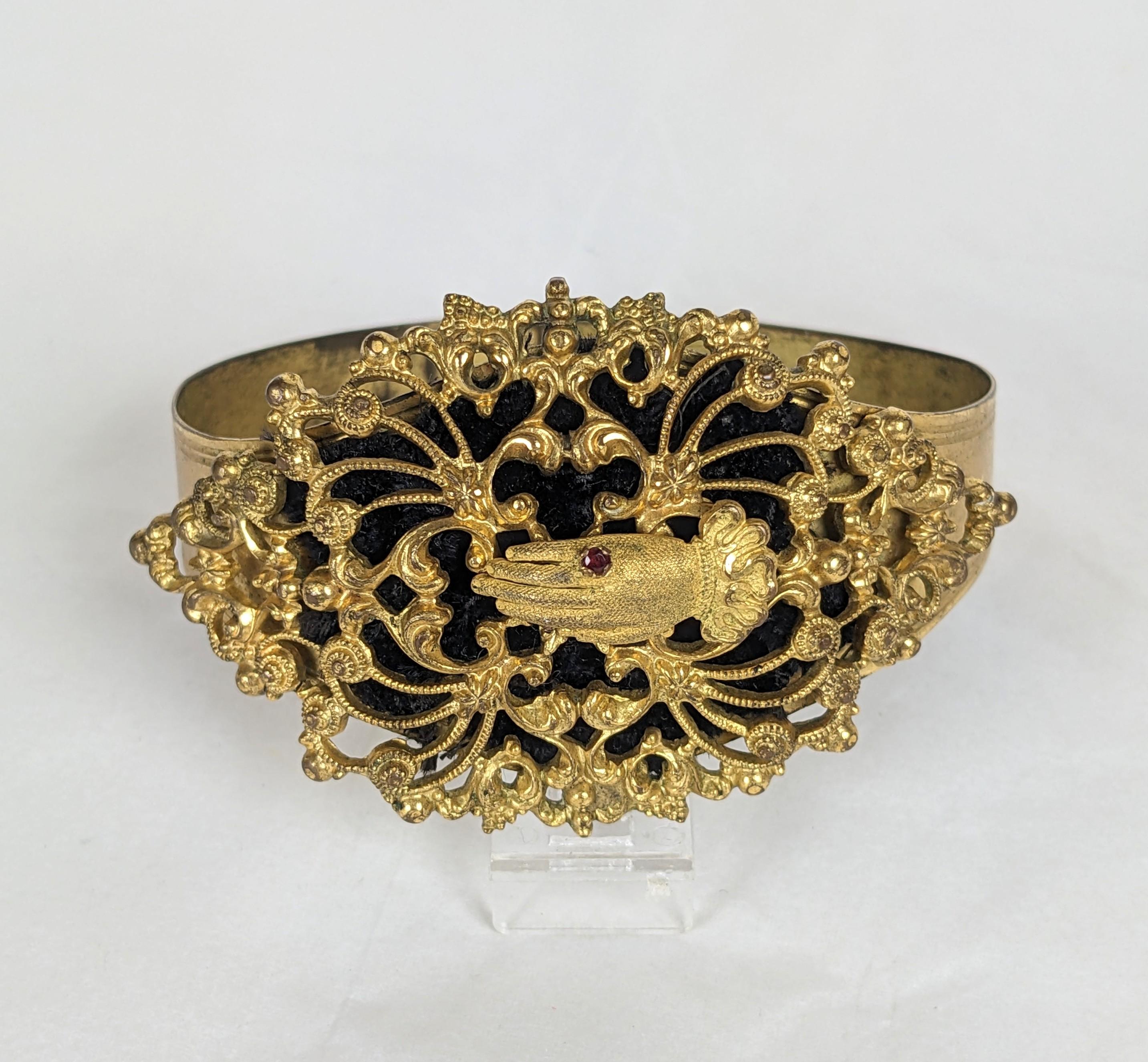 Unusual Victorian Gilt Hand Motif Cuff from the late 19th Century. A filigree motif is set on top of an adjustable cuff with hand and garnet ring motif . A piece of black velvet is placed underneath for contrast. 1880's. Motif 2.75