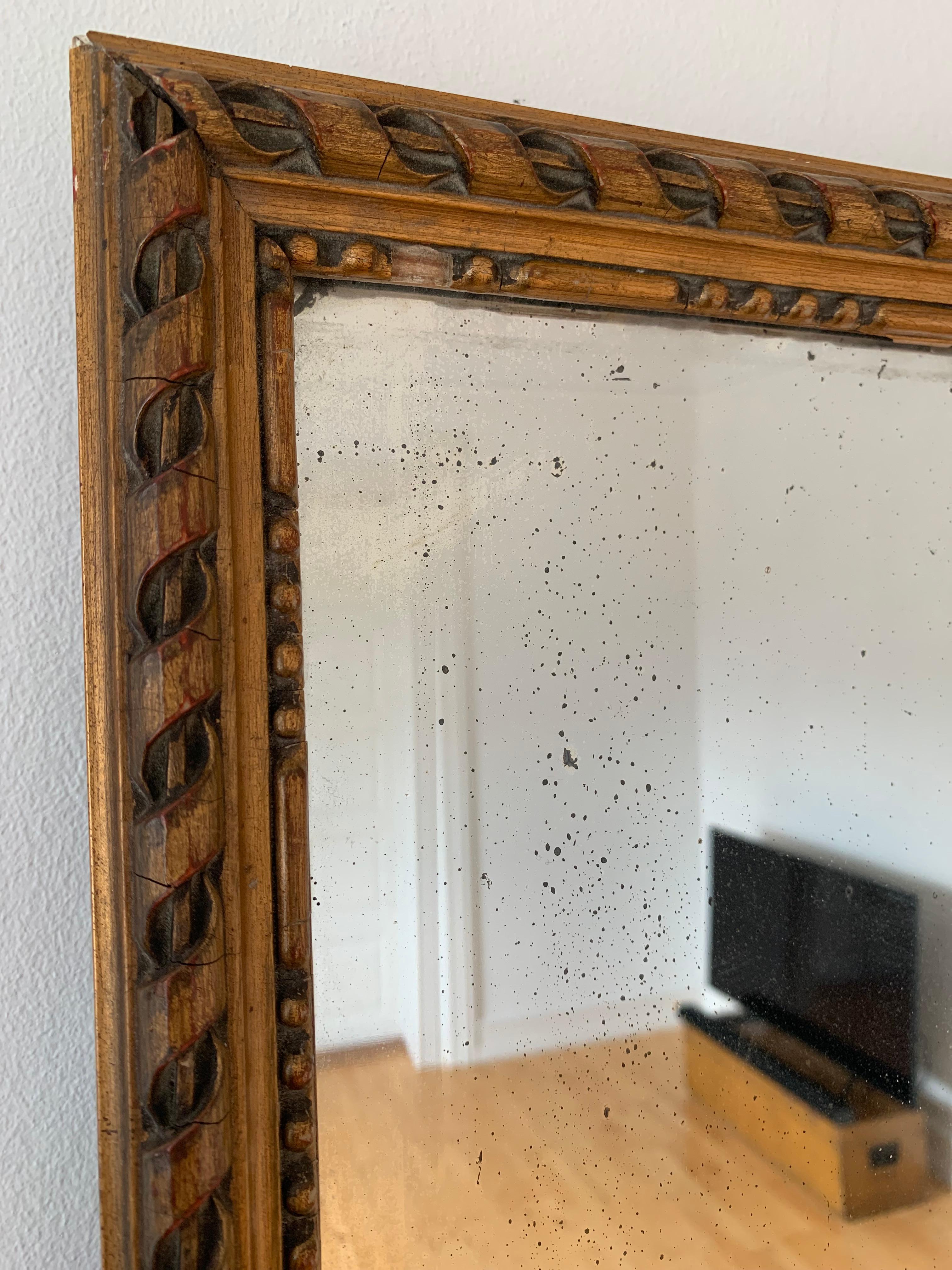 This elegant Victorian mirror features a richly carved and gilded rectangular frame with a beautifully weathered patina, revealing subtle hints of the red background beneath. A delicate pearl edge runs along the entire frame, enhancing its classic