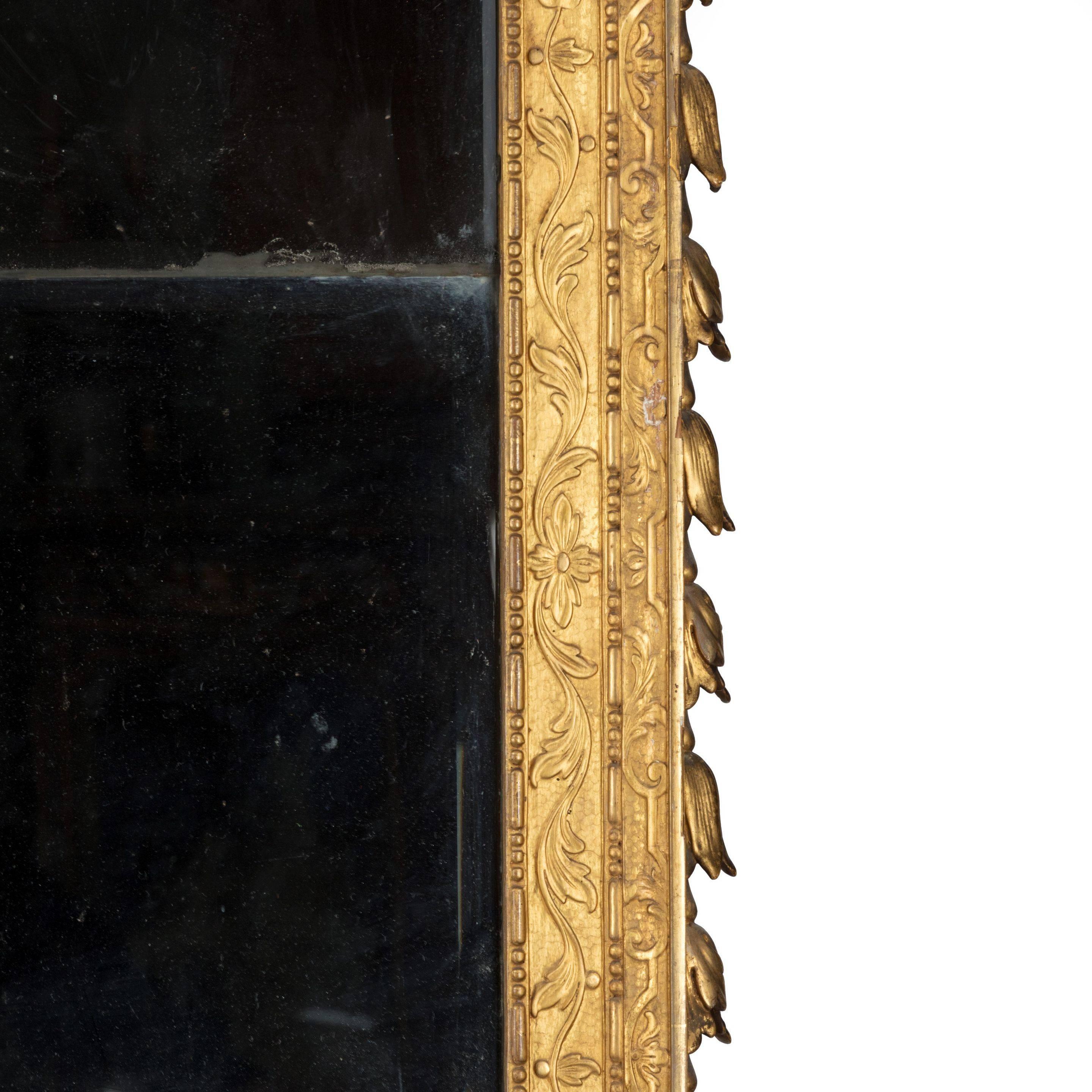 An elegant Victorian giltwood mirror after a design by William Kent, of slender rectangular form, decorated with both high relief and shallow carving, the broken pediment comprising a central cartouche flanked by two scrolls with trailing flower