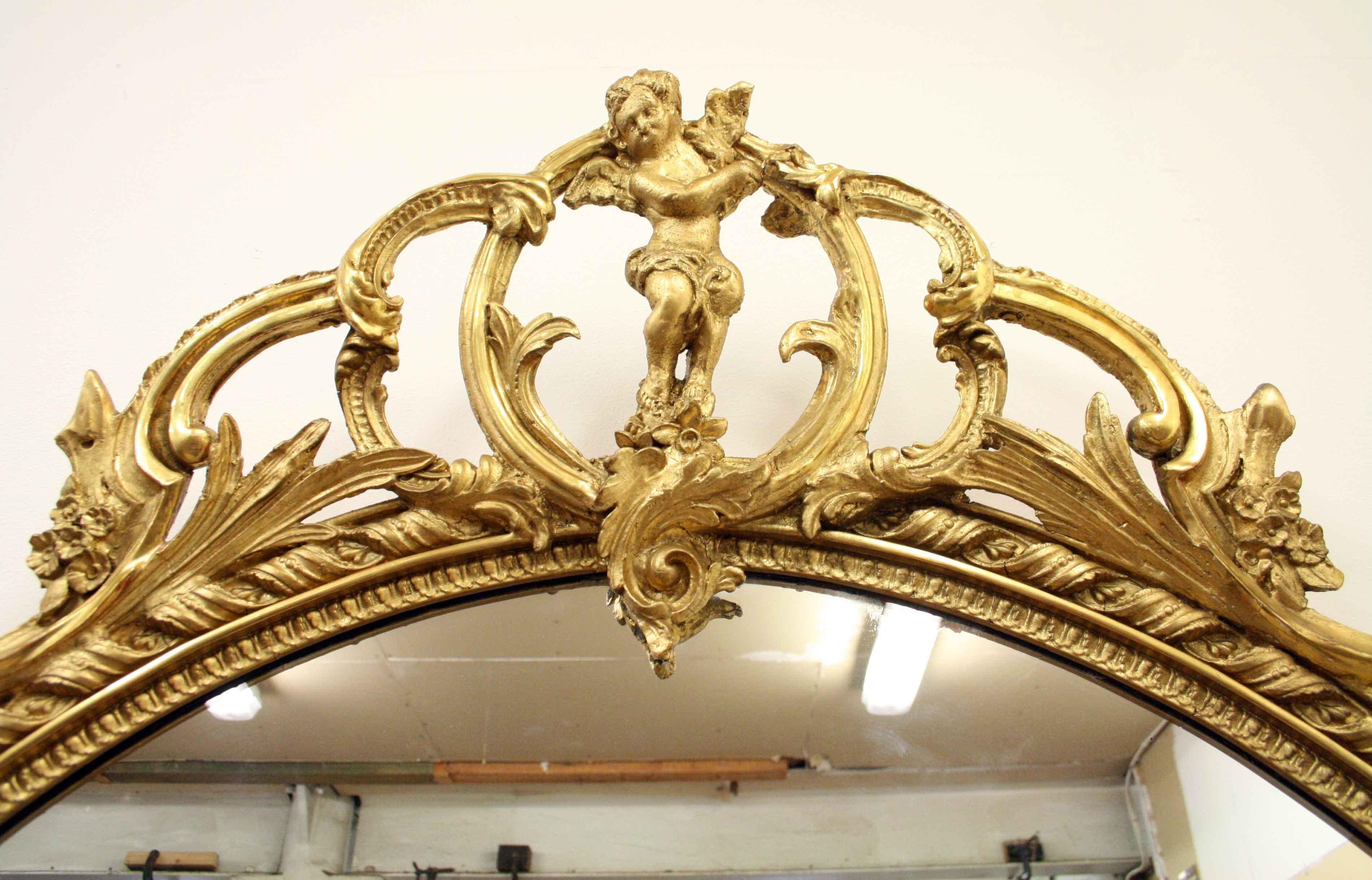 Victorian giltwood overmantel mirror of generous proportions, circa 1870. The stylish open fretwork pediment is surmounted by a cherub, held in place by Rococo carved gesso which tapers down the top of the mirror. There are two types of gilding on