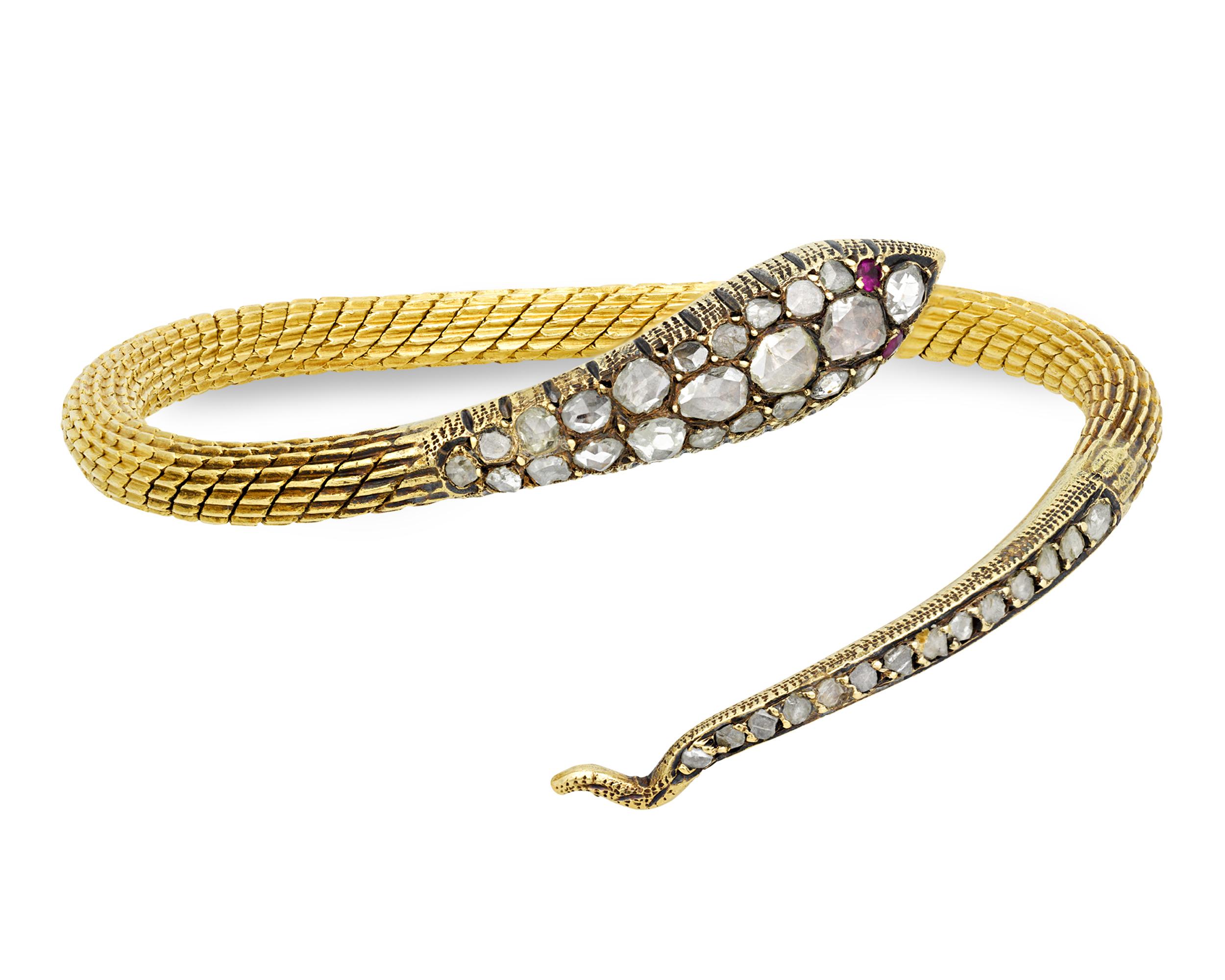 This eye-catching 18K yellow gold bangle bracelet takes the form of a slithering snake studded with diamond scales and brought to life with ruby eyes. Serpents became highly fashionable in jewelry design beginning in the mid-19th century, appearing
