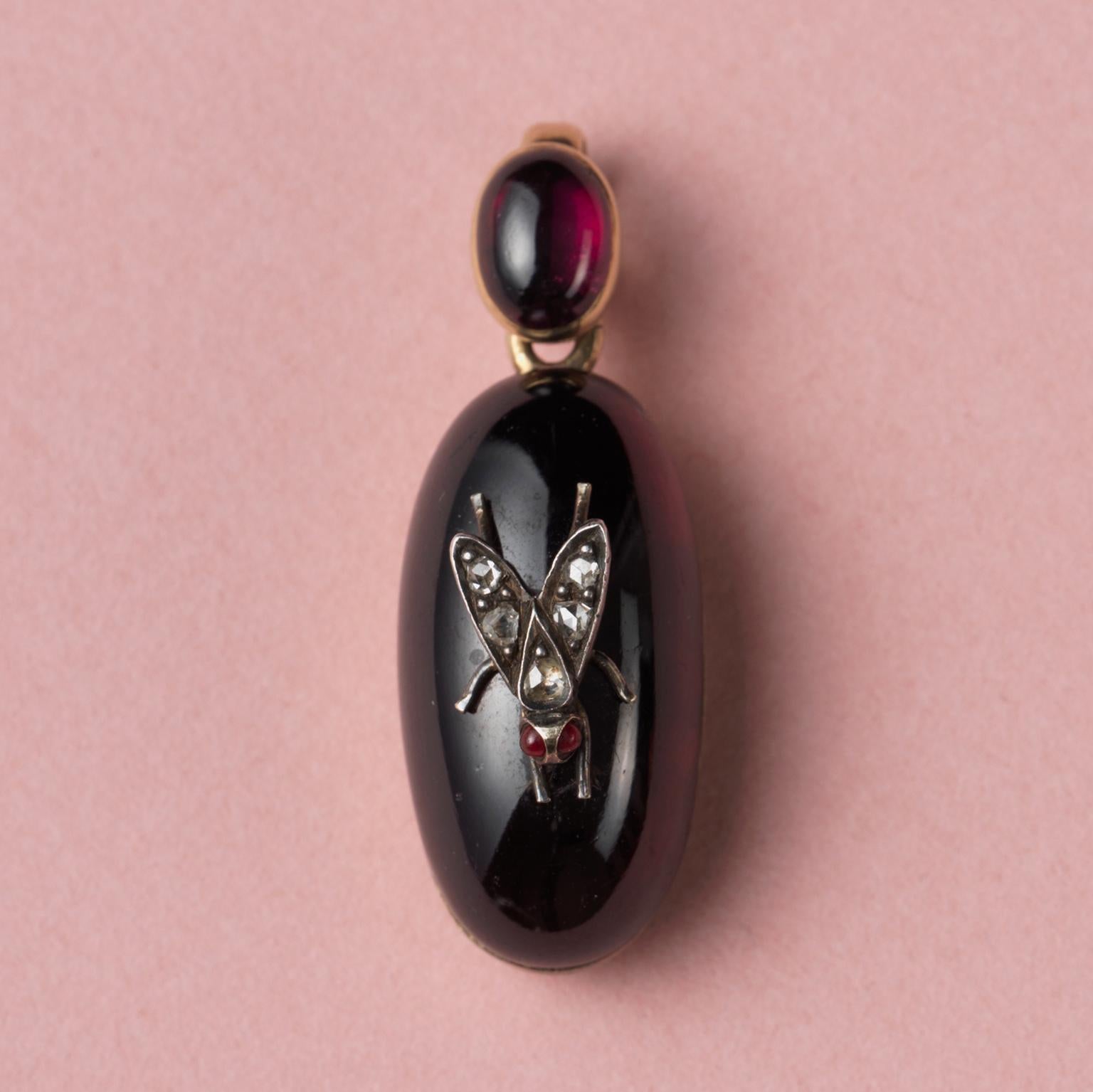 A 14-carat gold locket with a larger oval, cabochon-cut garnet decorated with a silver and diamond fly; the hoop is also set with a smaller cabochon-cut garnet, at the back is an oval locket with one glassed compartment. England, end 19th