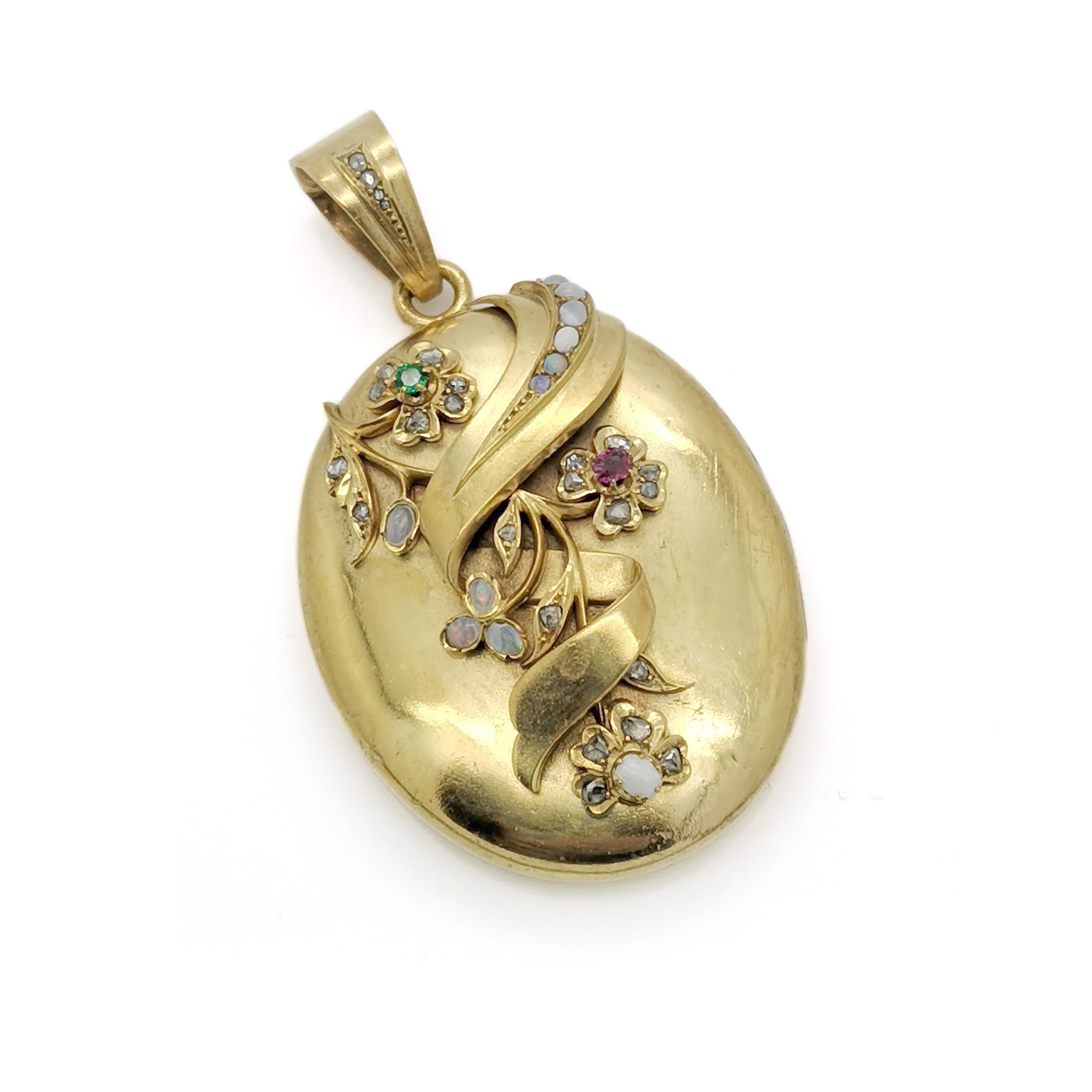 A Victorian gold and gem set locket, the oval locket set with opals, a ruby and an emerald in a flower motif, opening to two compartments. Circa 1875.