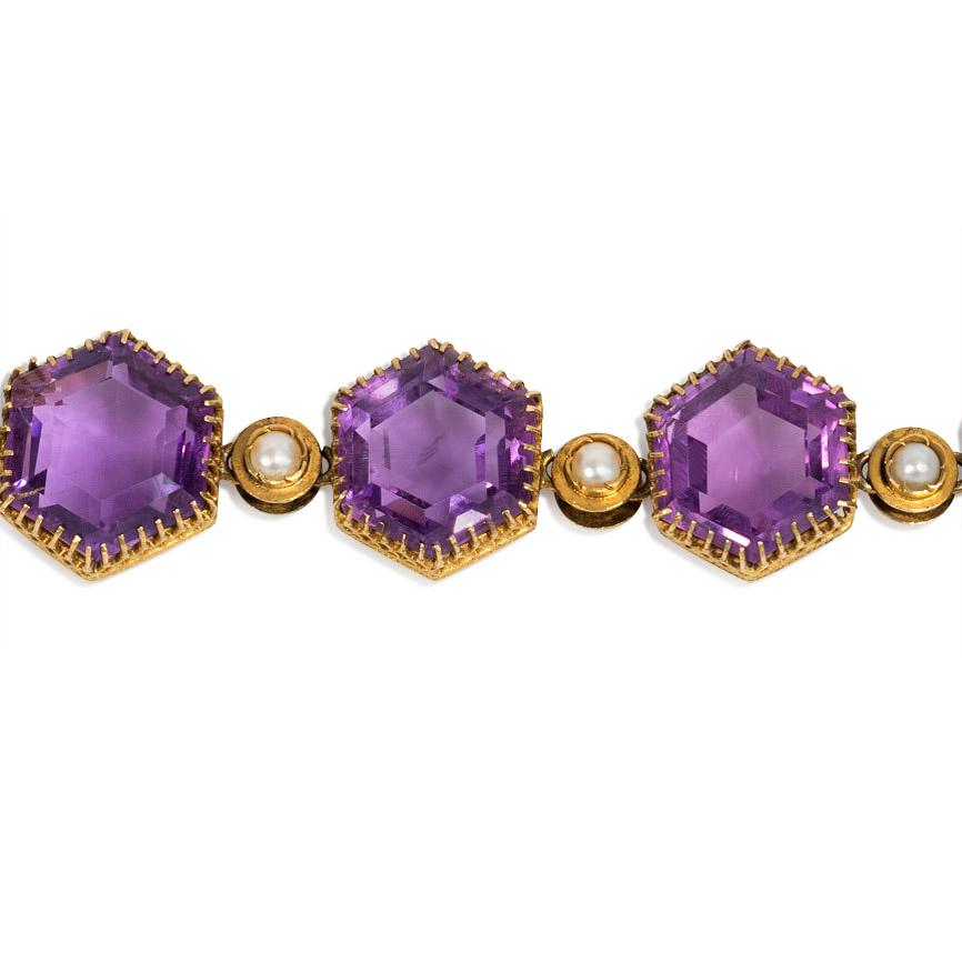An antique bracelet of tapering hexagonal-cut amethysts with alternating half-pearl spacers, completed by a gold box clasp decorated with wirework, in 15k gold.  England