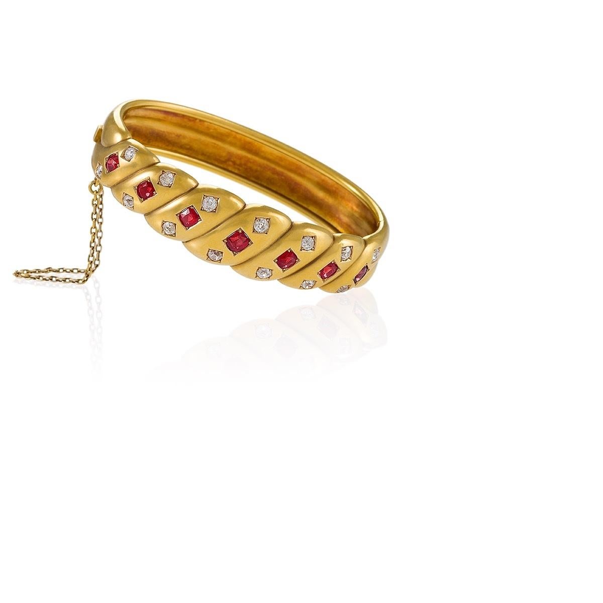 A late Victorian gold bangle bracelet with rubies and diamonds. The bangle bracelet features a simple and elegant twisted rope design that is energized by the 7 beautifully matched rubies, approximately 2.00 carats total weight, and 14 old mine cut