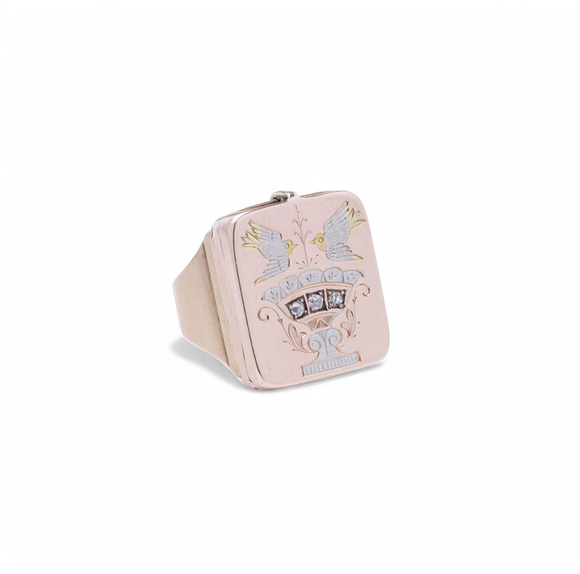 A beautifully crafted Victorian-era locket ring, designed with a hidden hinged compartment, a sentimental feature often used for keepsakes or mementos. The square-shaped face is finely engraved with a delicate urn and two birds in flight,