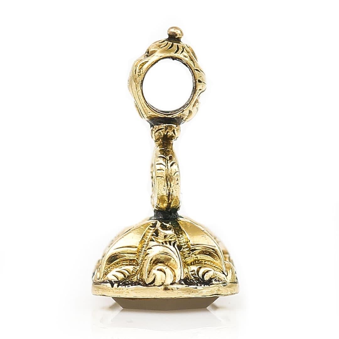A delightfully dainty and rare Victorian 9ct gold fob seal that has a masterfully carved forget me not engraved into a shield chalcedony base. The body of the fob has deeply chased panels with a lyre motif at its centre and a small loop to its peak