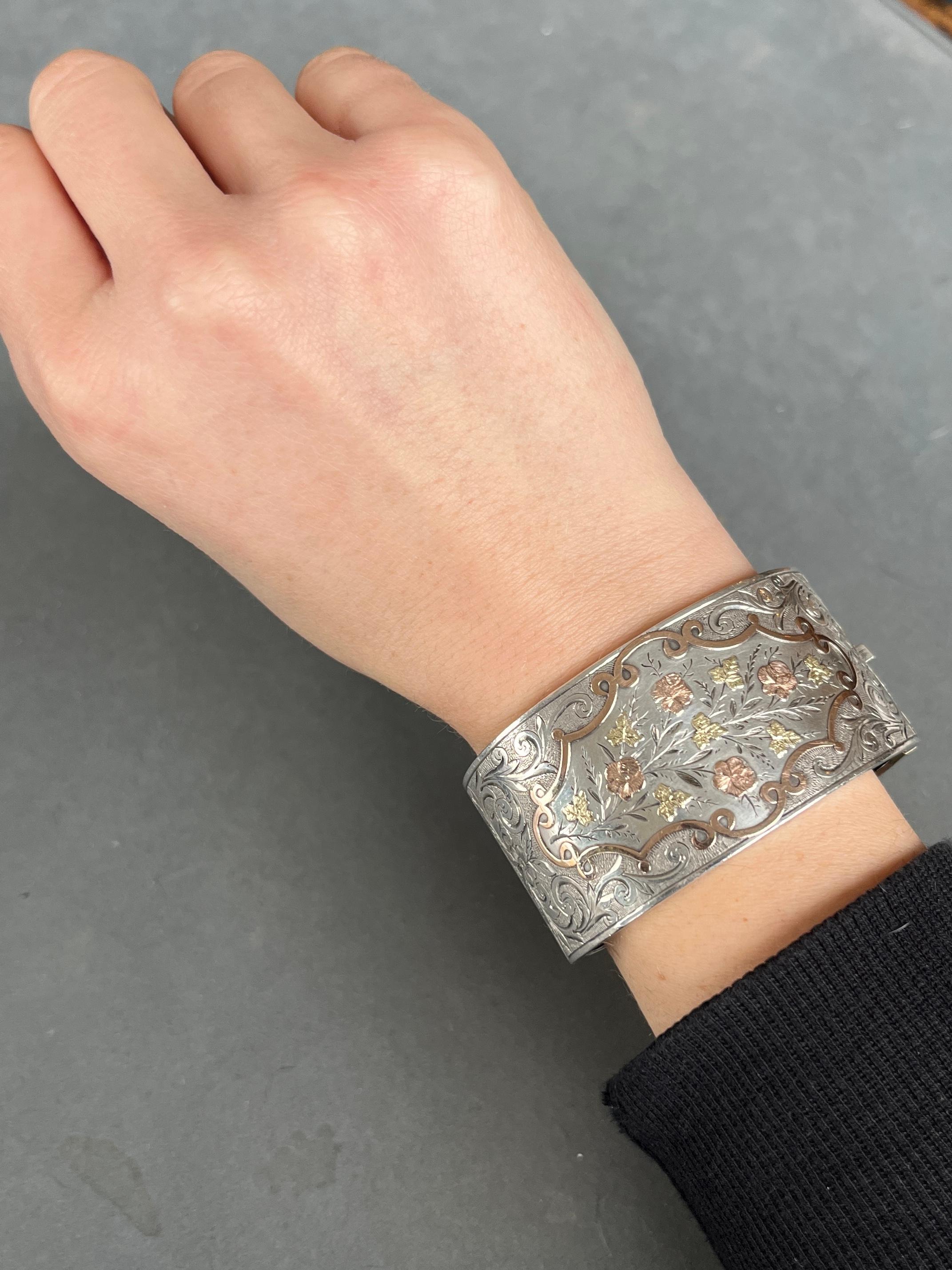 An exquisite antique bangle from the Victorian era circa 1880. Decorated with superb hand-chased detailing with yellow and rose gold overlay scroll, leaf and flower motifs. Modelled in silver.

Inner diameter: 5.7cm (from hinge to clasp)
Bangle