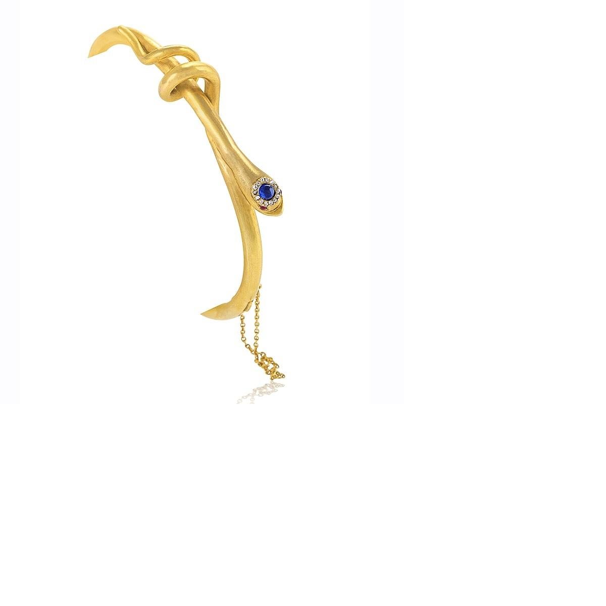 An English Victorian 18 karat gold hinged snake bangle with diamond, sapphire and ruby. The head is a cabochon blue sapphire that has the approximate weight of .15 carat surrounded by .12 carat of rose cut diamonds with 2 cabochon ruby eyes that