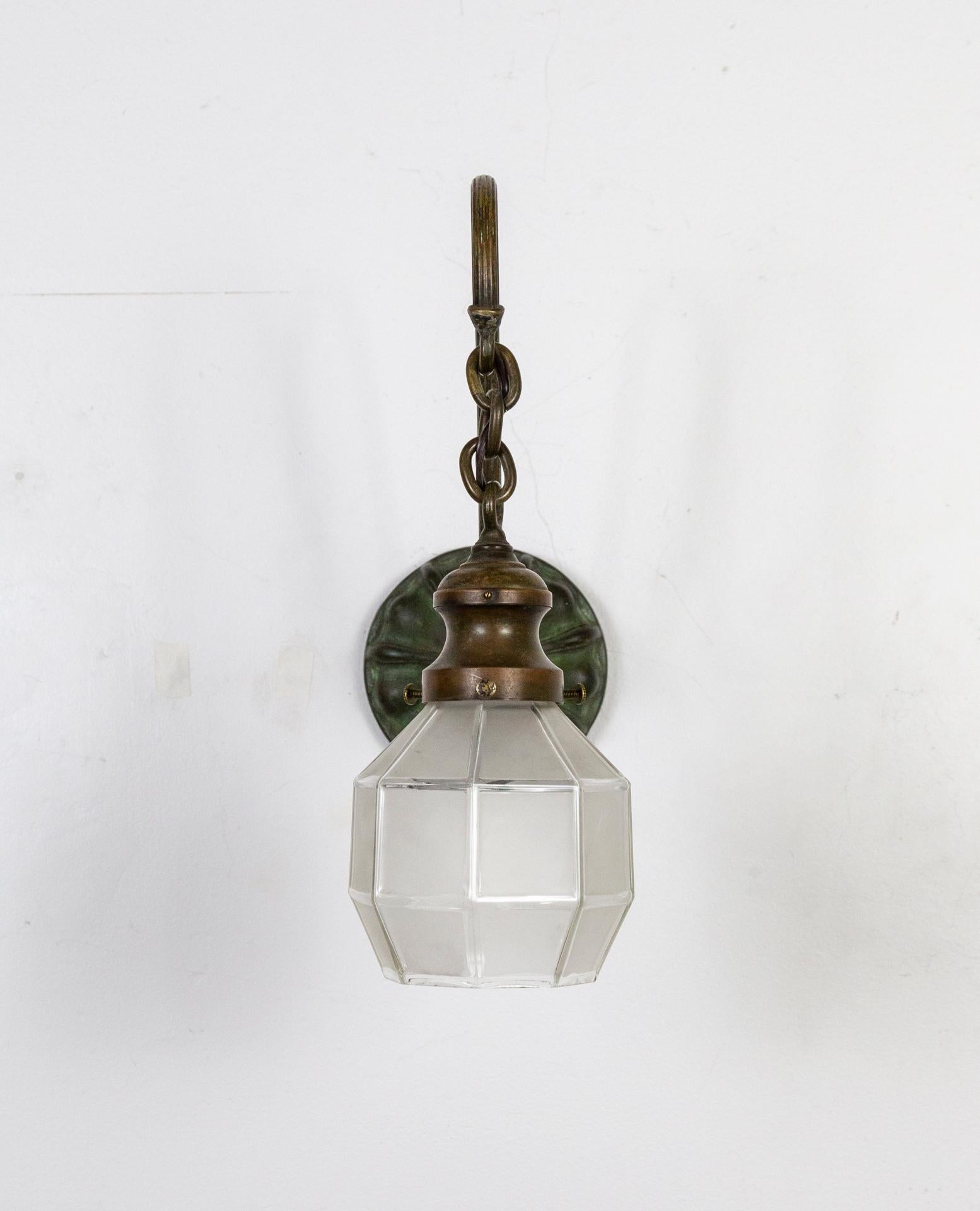 A pair of Victorian Era wall sconces with reeded, swooping arms and Sheffield style back plates. A rich patina throughout in verdigris and bronze tones with chain and shade holder adding to the overall shape. The shades are soft edged, faceted,