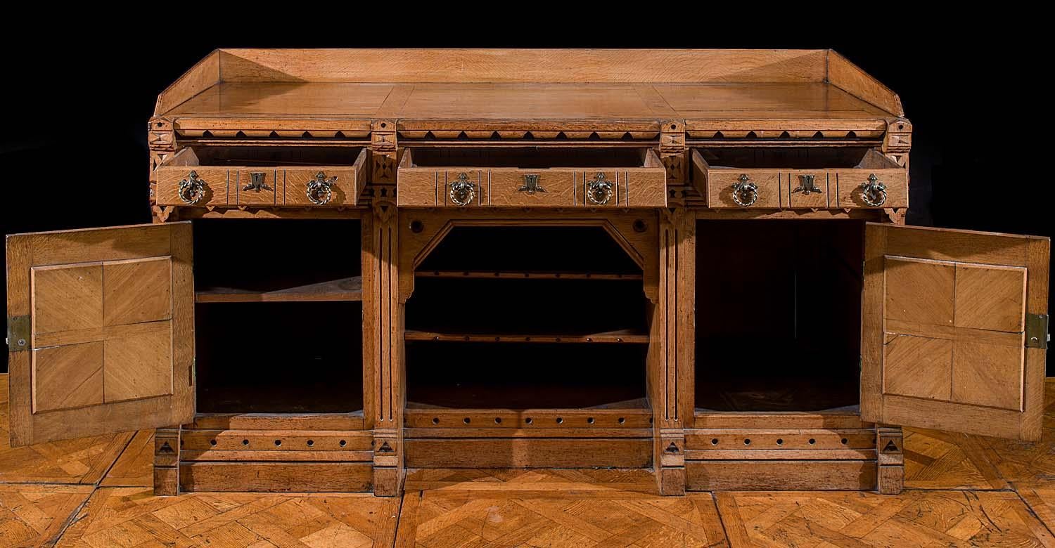 A Gothic Revival oak and inlaid ebony Victorian sideboard attributed to the renowned English furniture designer Charles Bevan (1820s-1882).

The undercut top shelf, with a raised three quarter gallery, rests above three neat drawers beneath which