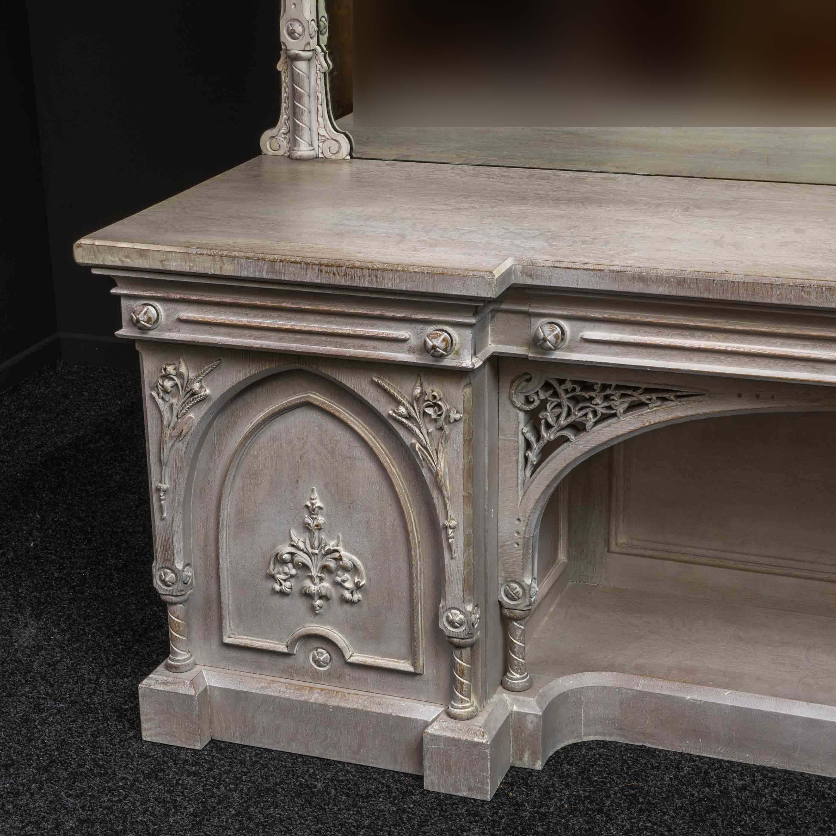 A Gothic limed oak sideboard from the Victorian period. The huge mirror has central cartouche to the frame and the original carved finials, whilst the base has beautiful Gothic arched doors with crisp carvings of foliage and ears of wheat. The