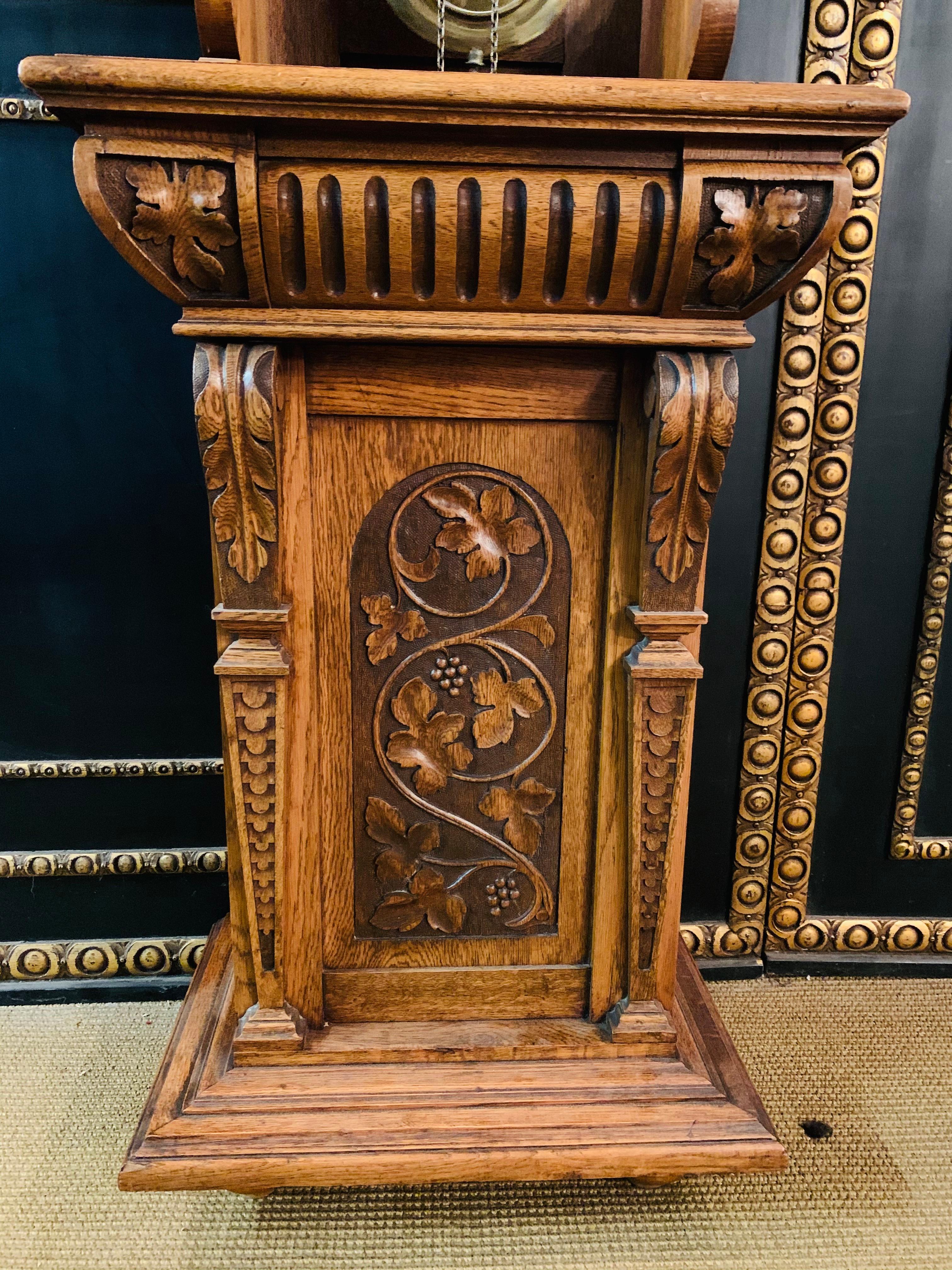 Grandfather clock made of oak Victorian style circa 1880 cantilever, elaborately carved, with grapevines and oak leaves, crowned with a gallery of turned columns, 2-colored dial with Arab. Numerals and blackened hands, clockwork with 1/2 hour