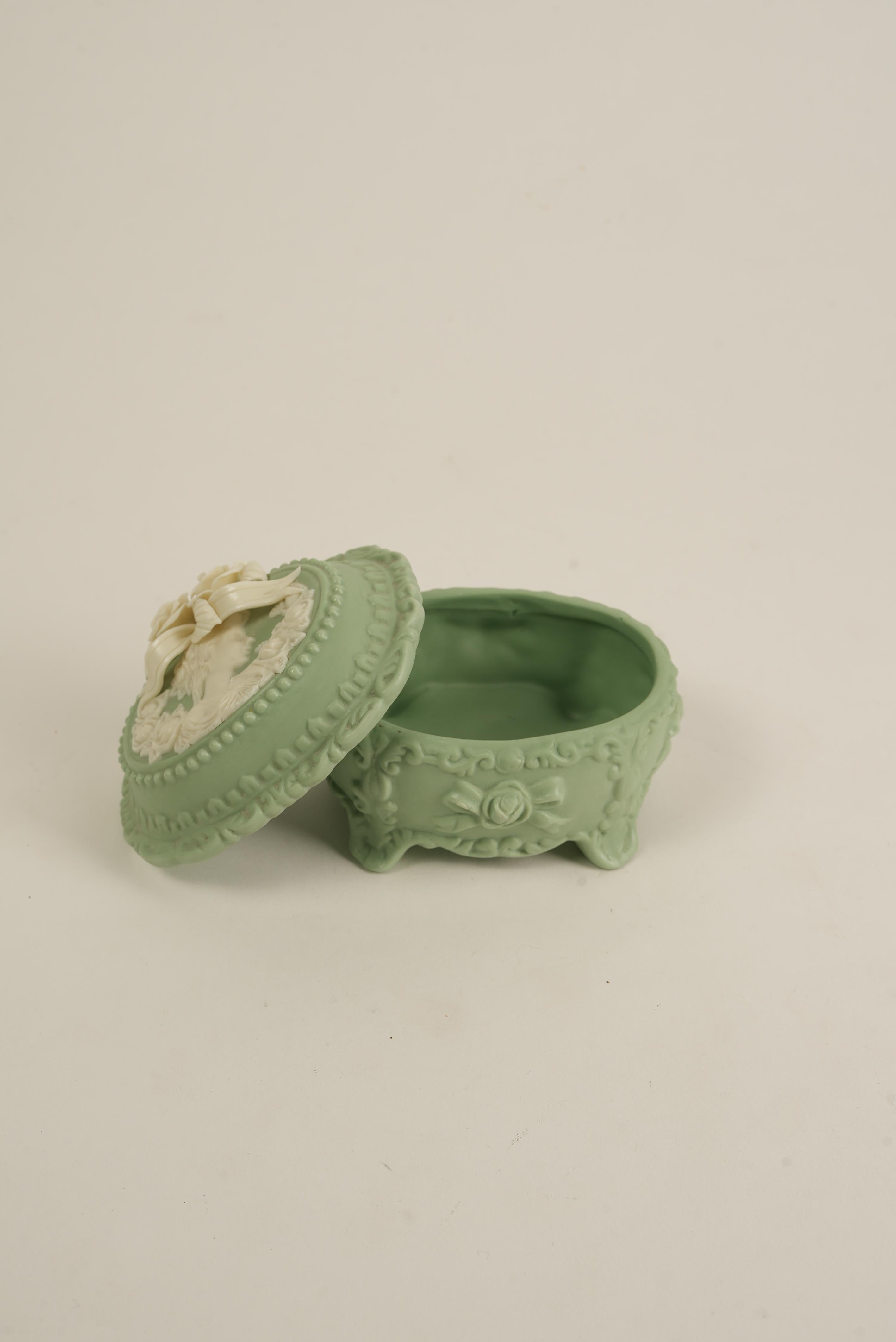Cette charmante boîte à bibelots vintage se distingue par son allure victorienne, ses détails en relief et son portrait en camée entouré de roses. Le délicat couvercle floral tridimensionnel de couleur ivoire ajoute un intérêt sculptural et