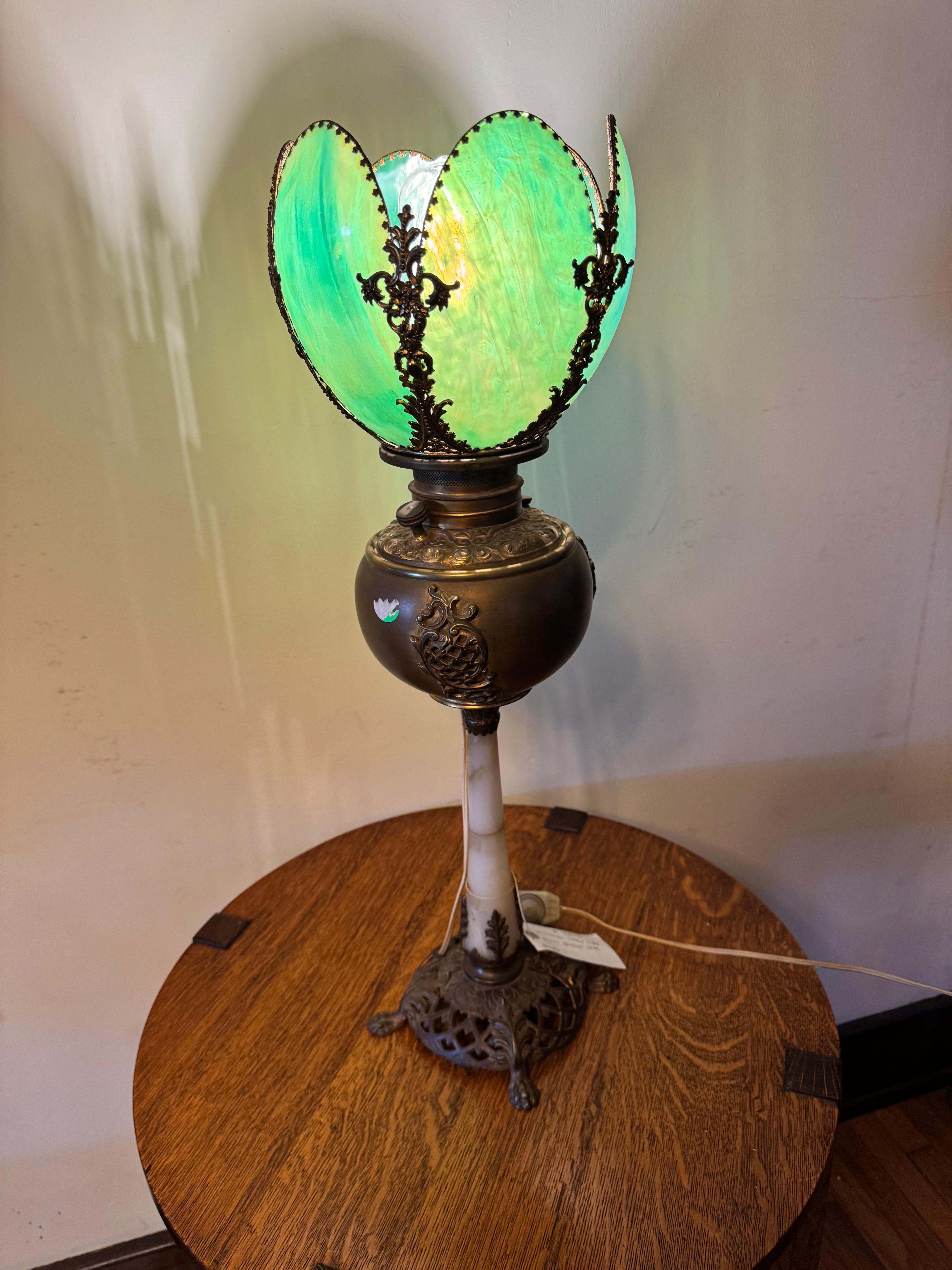 This is a striking Victorian Green Slag Glass Banquet Lamp from the early 1900s.  The lamp was originally an oil lamp that was wired for electric. The wire was run on the outside of the lamp (see photos) so the oil lamp tank was not damaged.  If you