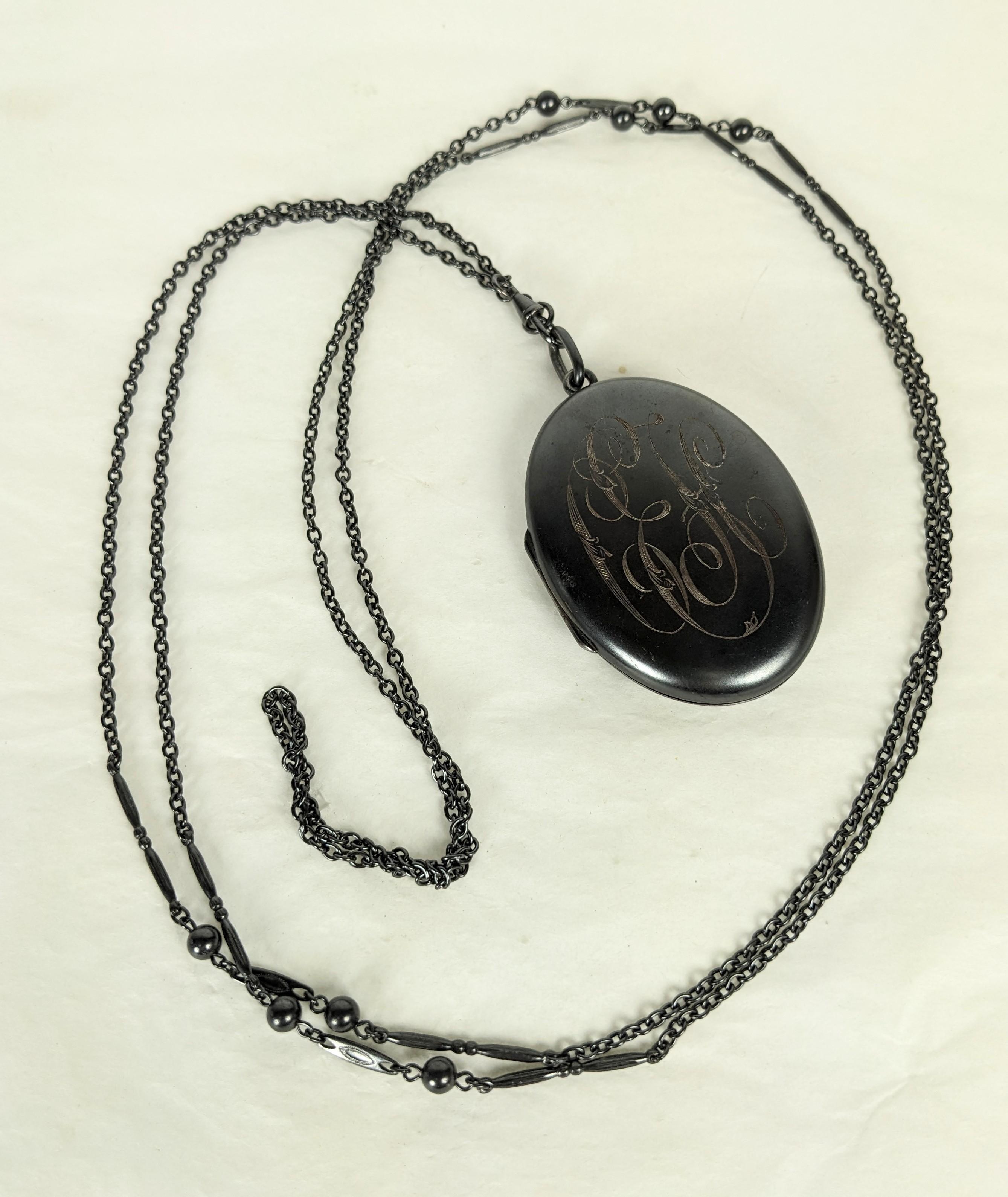 Lovely Victorian Gunmetal Locket and Long Chain from the late 19th Century. Original long chain interspersed with bar and bead sections. Original gunmetal hook and fittings. Large locket has scrolled engraving, hard to decipher with possibly 
