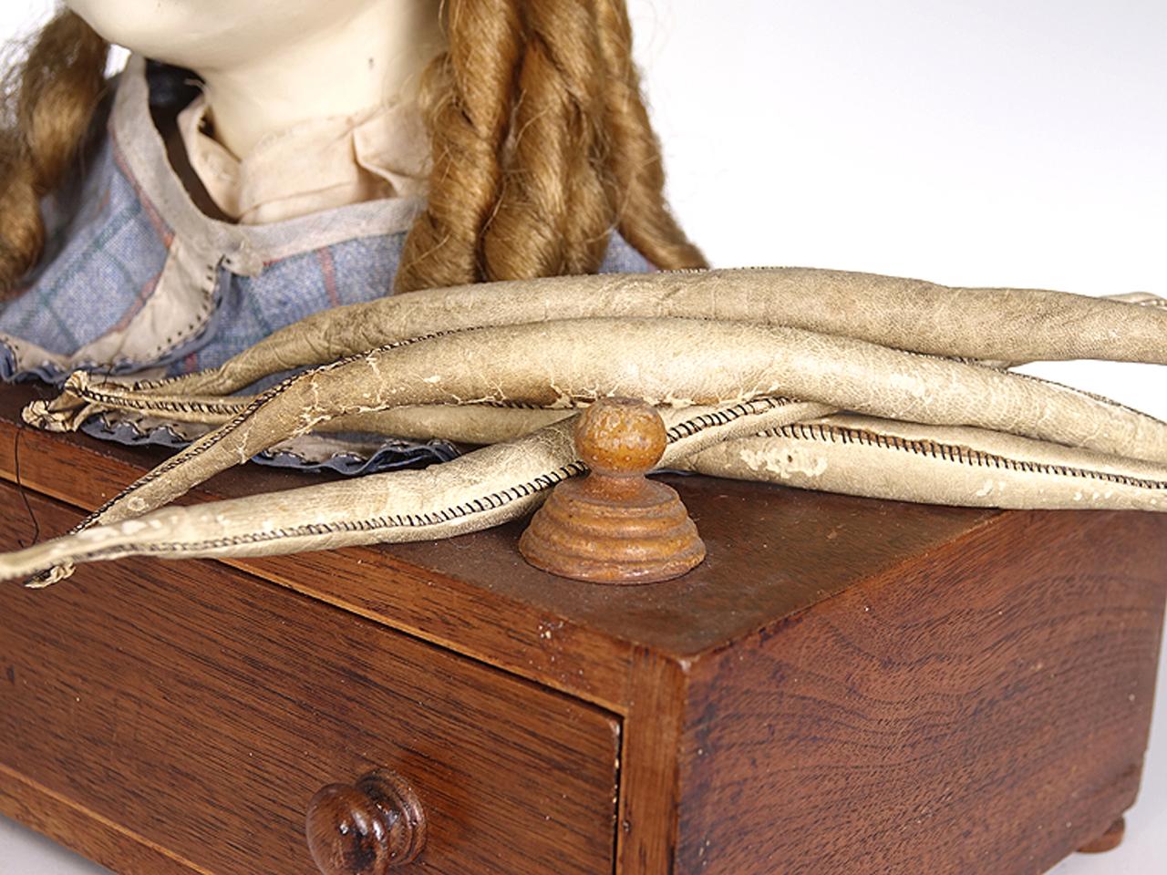 This is an early styling doll. When have you seen another dating to the 1800s. Its mounted to a cabinet with one draw. In the draw are a handful of worn original leather and horse hair rollers. Importantly the condition of the dolls hair is clean,