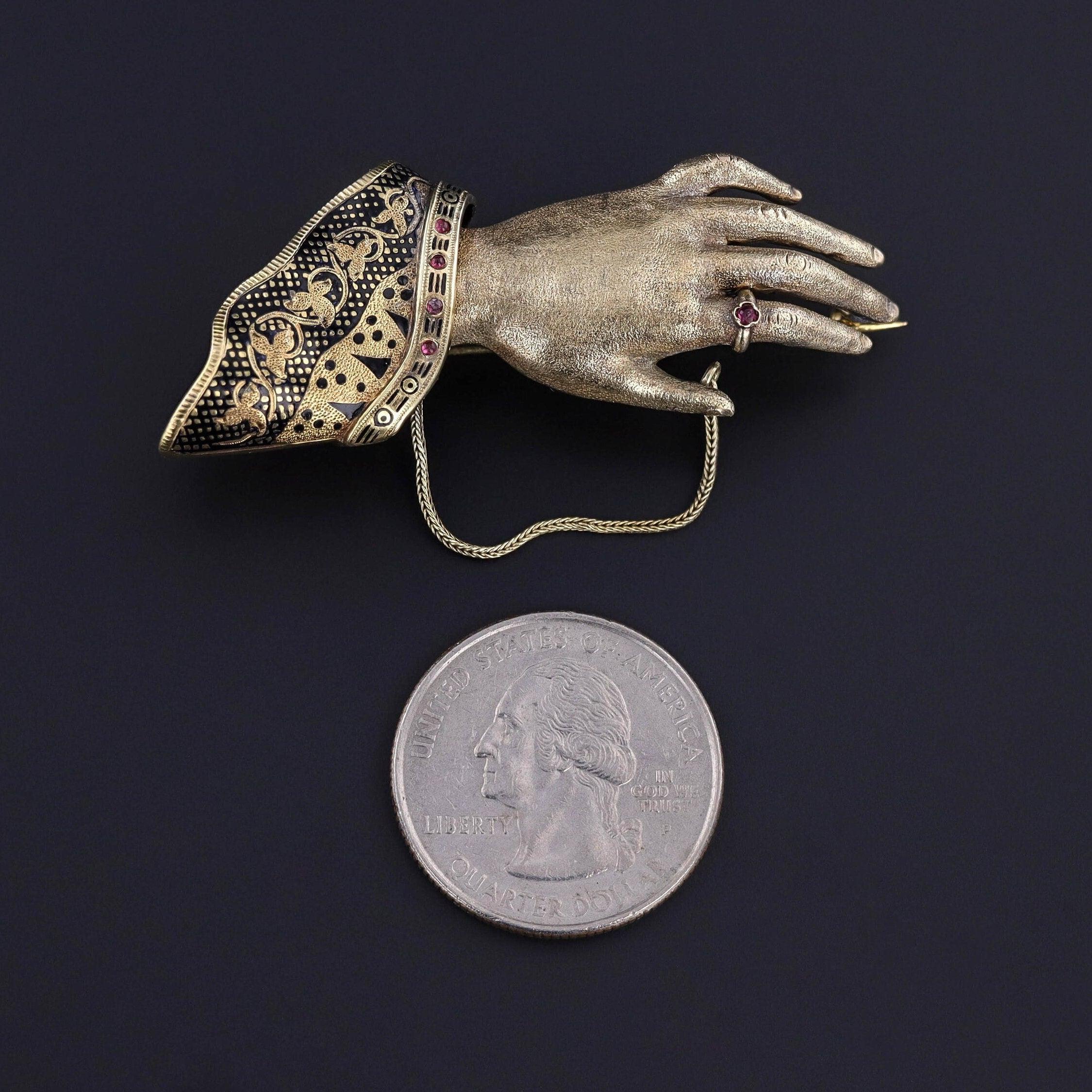 Questa rara spilla antica di epoca vittoriana (circa 1860) presenta una mano d'oro a 14 carati con un bracciale in pizzo smaltato nero e accenti in vetro rosso.

Il pezzo misura 1,5 pollici per 2,2 pollici di larghezza ed è in ottime condizioni. Il