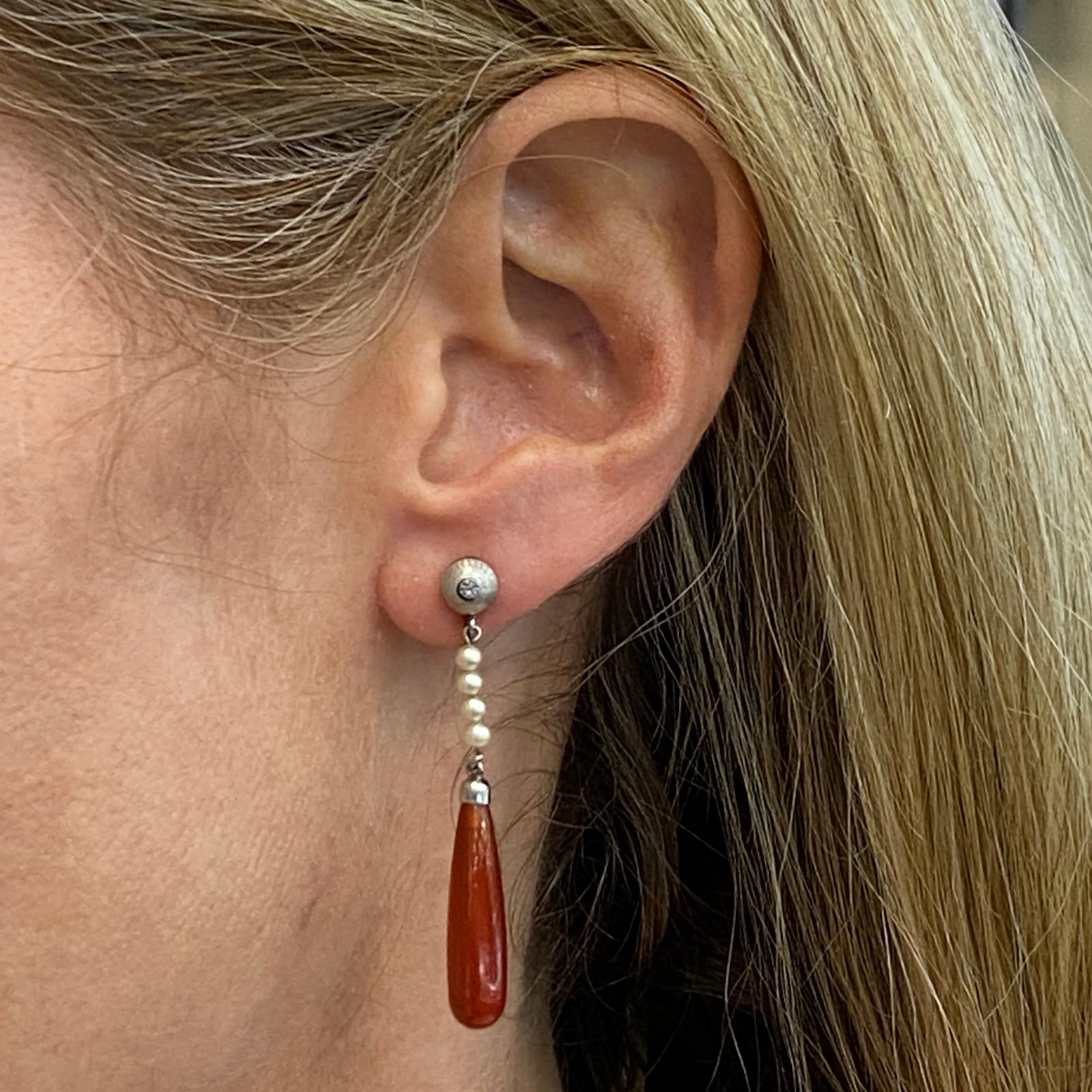 Original Victorian carnelian drop earrings fashioned in 14 karat white gold. The earrings feature hand carved carnelian gemstones and pearl drops. The earrings measure 1.5 inches in length and are crafted with screw on clip backs. 