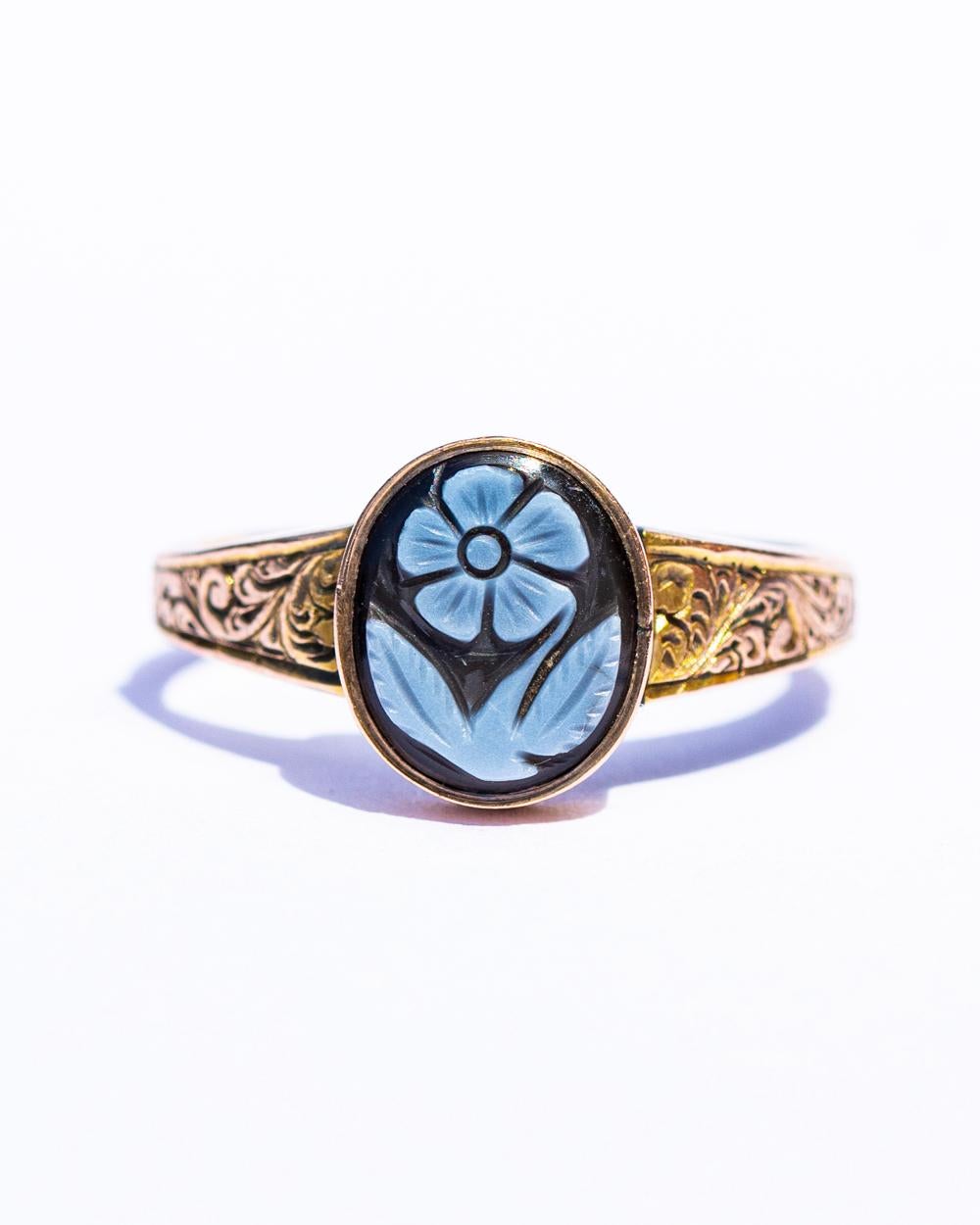 An early Victorian hard stone memorial ring, with an oval carved sardonyx forget-me-not, rub set to the head with a glazed locket verso, curved shoulders and a later shank, modelled in 22carat gold 

size N 1/2 or 7
10 x 18mm, 

2.82g