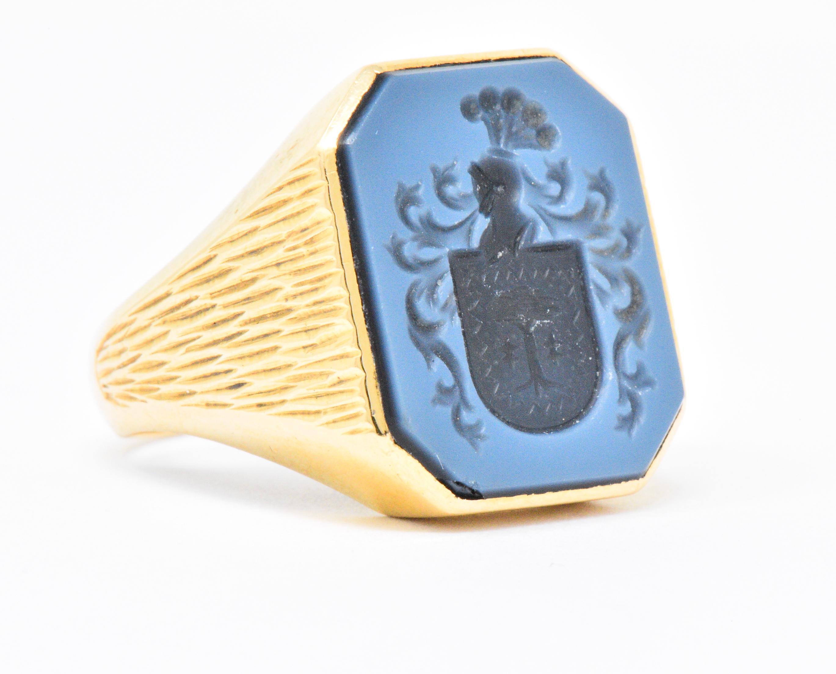 Centering a cut-corner banded onyx measuring approximately 18.0 x 14.6 mm

Intaglio depicting a plumed knights helmet atop a shield centering a tree with scrolling detail

A delicate bluish hue is produced by the thin layer of white over